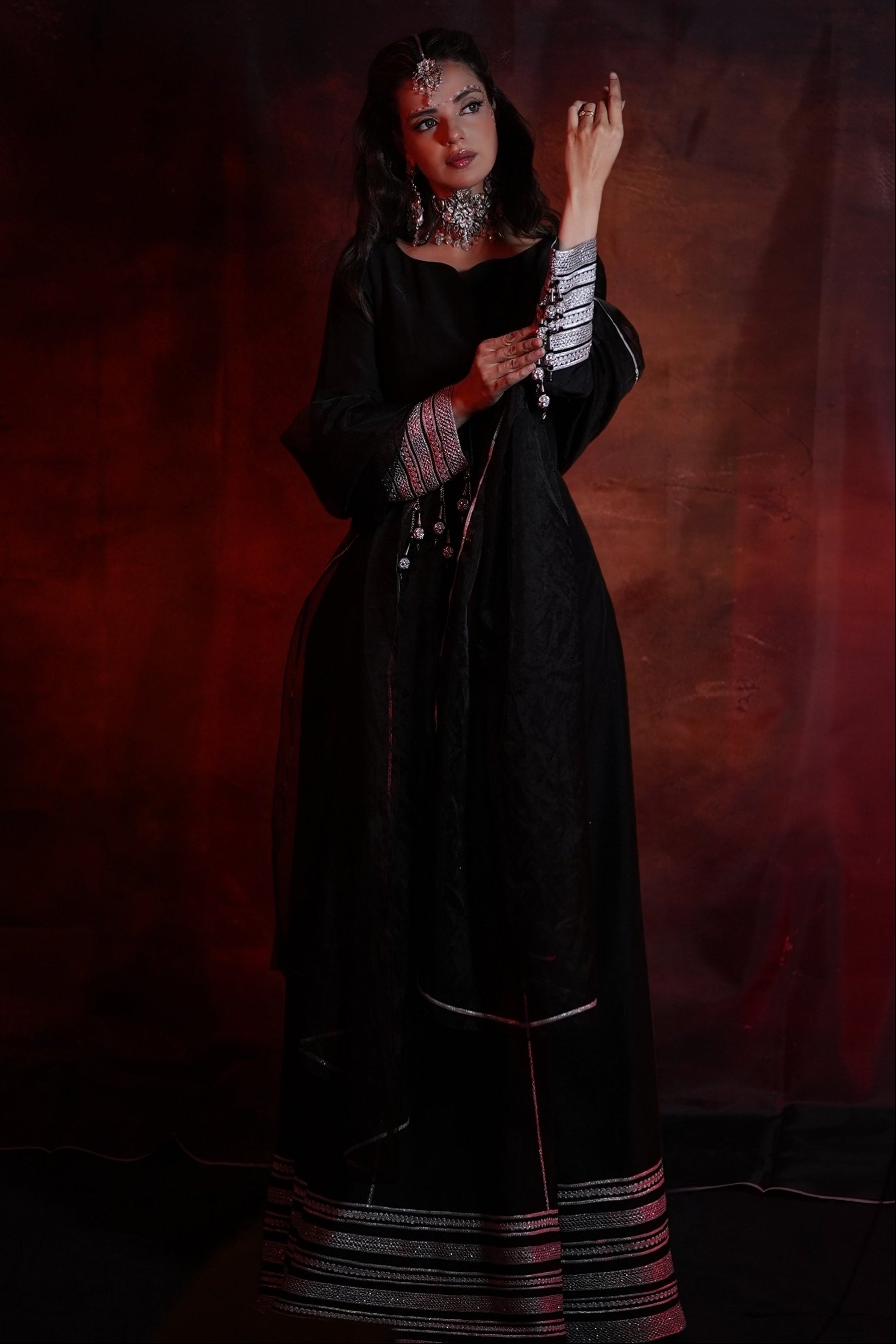 Woman in a dark, long dress with intricate details against a red-brown background