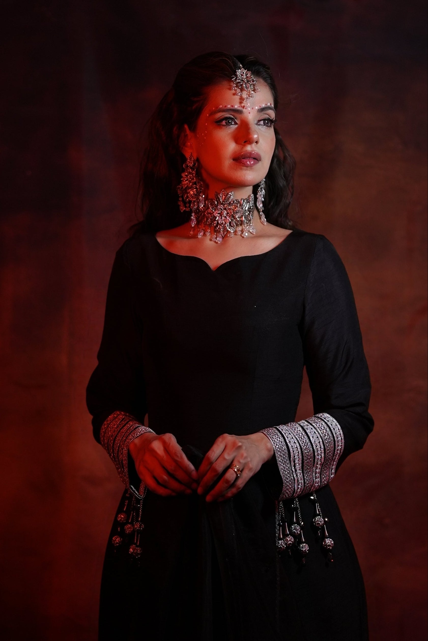 Woman in a black traditional outfit with jewelry against a brown background