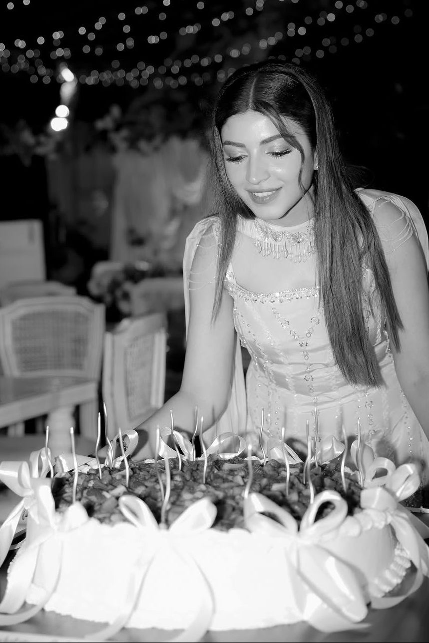 Woman in a white dress standing next to a large cake with candles at an outdoor event.