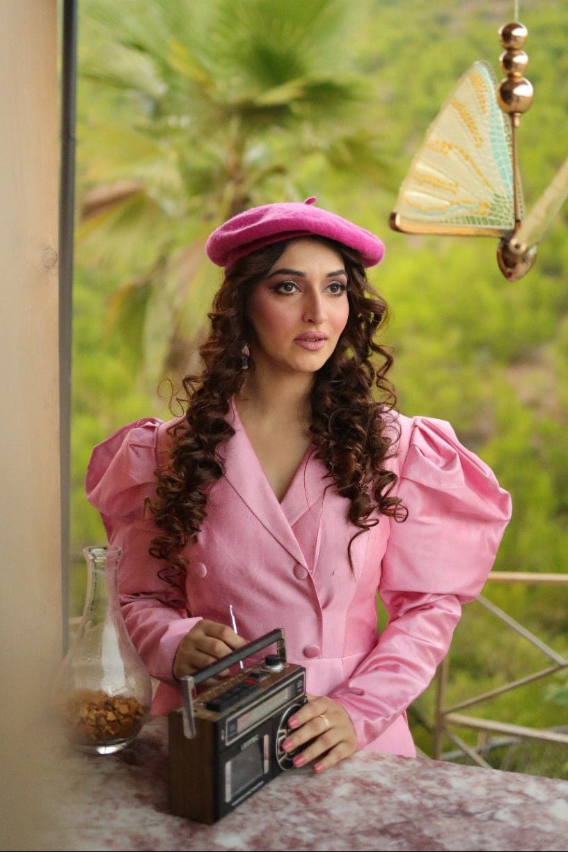 Woman in a pink outfit with a matching hat sitting on a balcony with a scenic view.