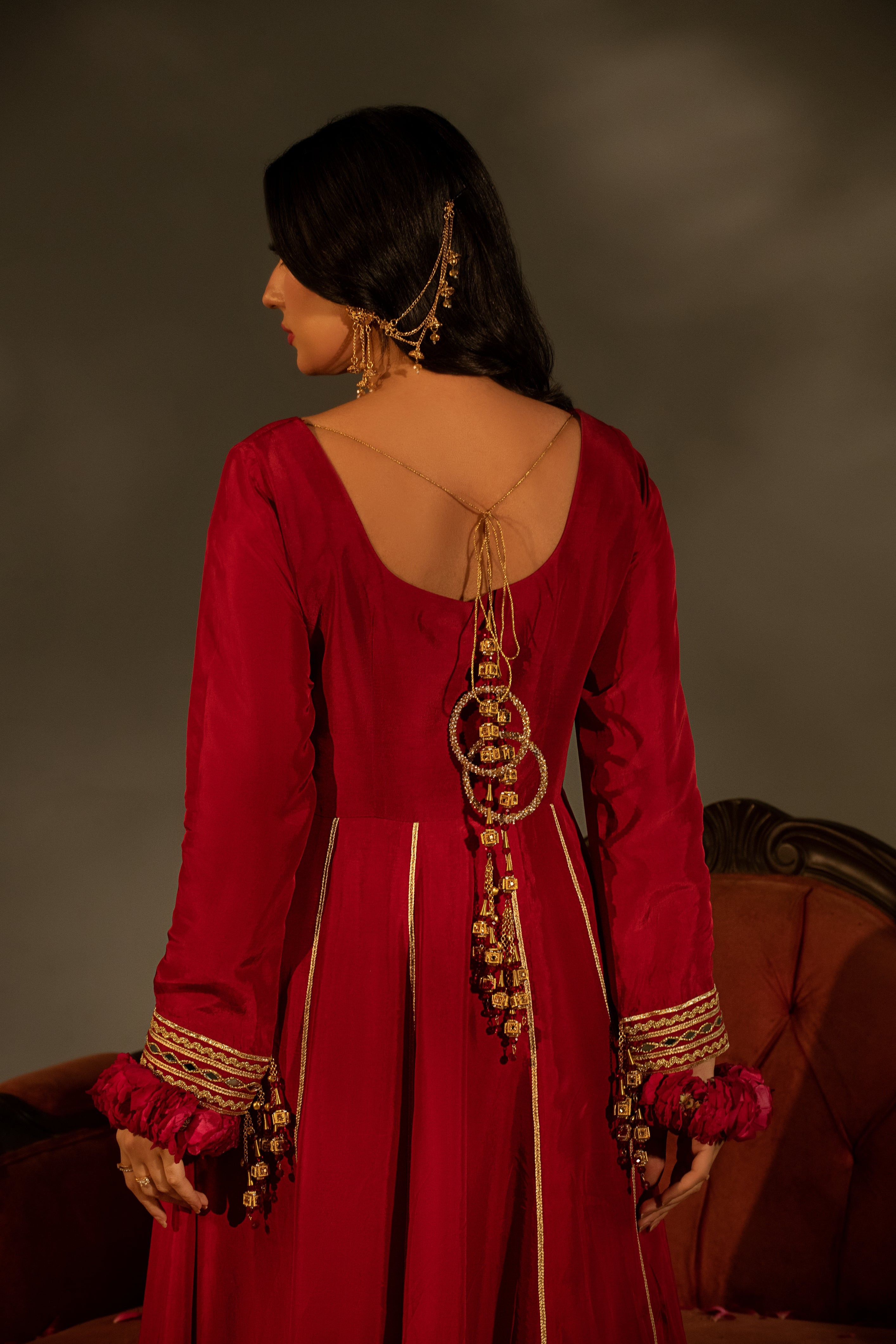 Woman wearing a red traditional outfit with gold details, standing against a dark background.