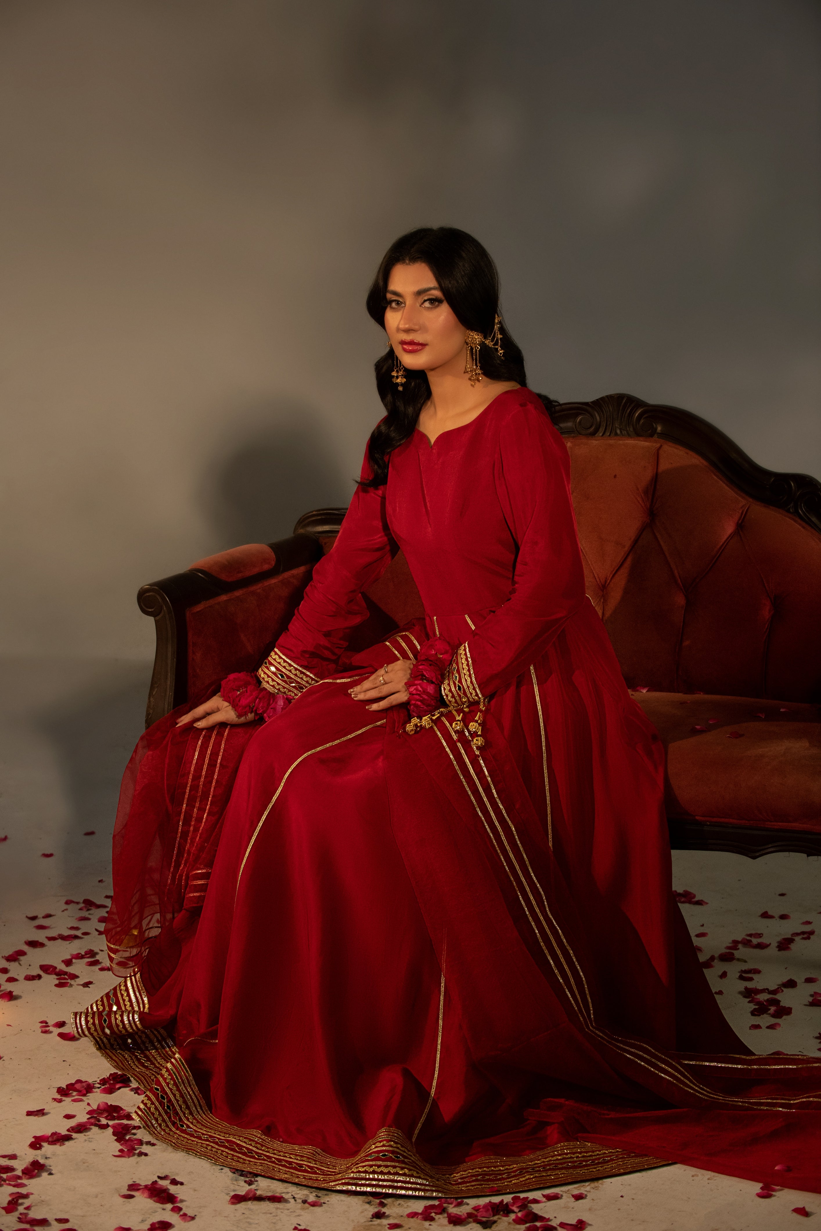 Woman in a red traditional outfit sitting on a brown couch with a gray background