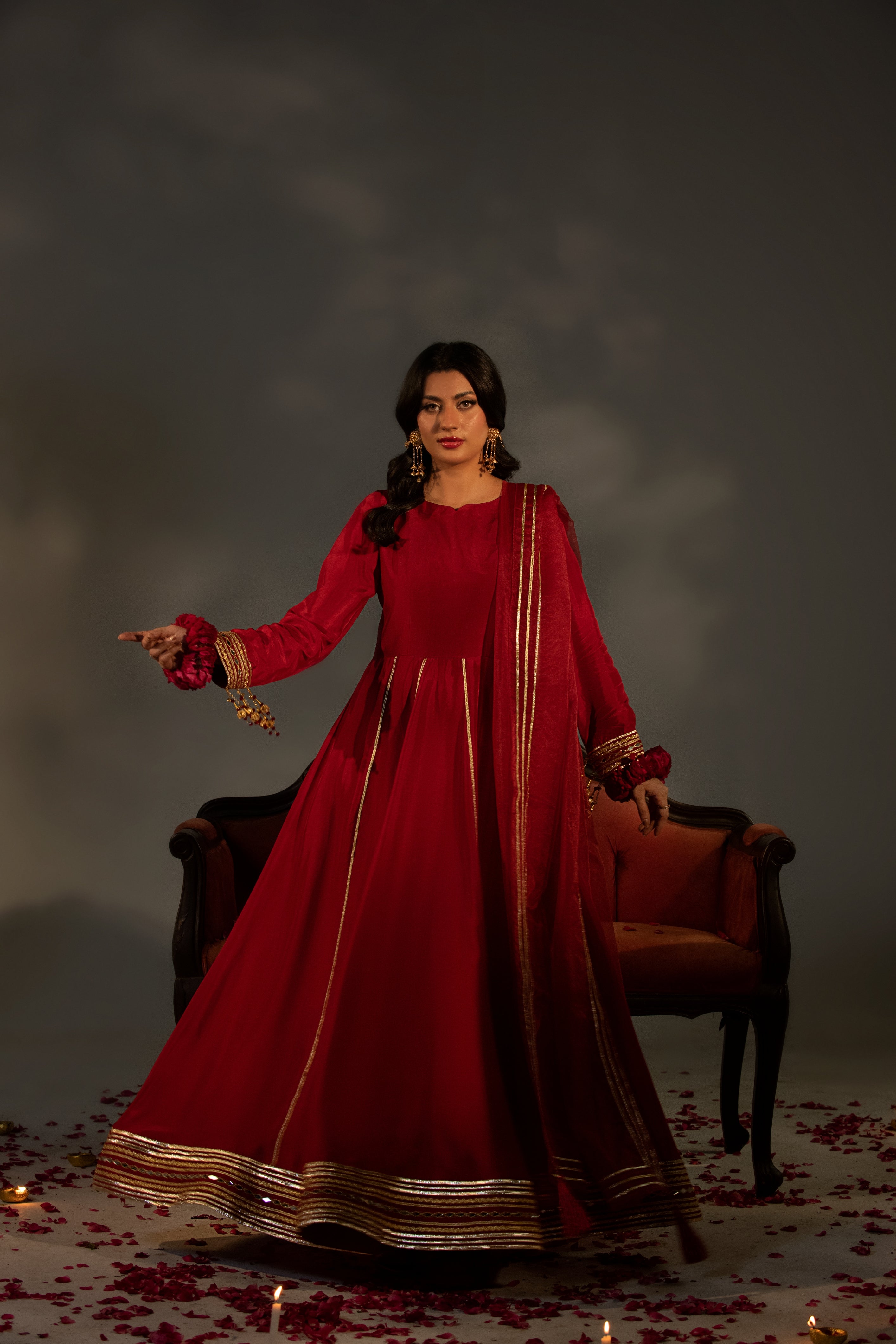 Woman in a red traditional outfit standing in a dimly lit room with a dark background.