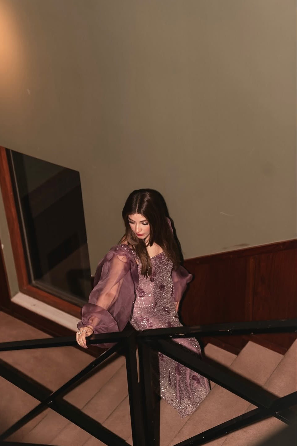 Woman in a purple dress standing on a staircase with a mirror in the background