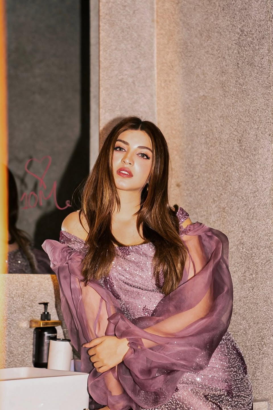Woman in a purple dress sitting in a room with a textured wall.
