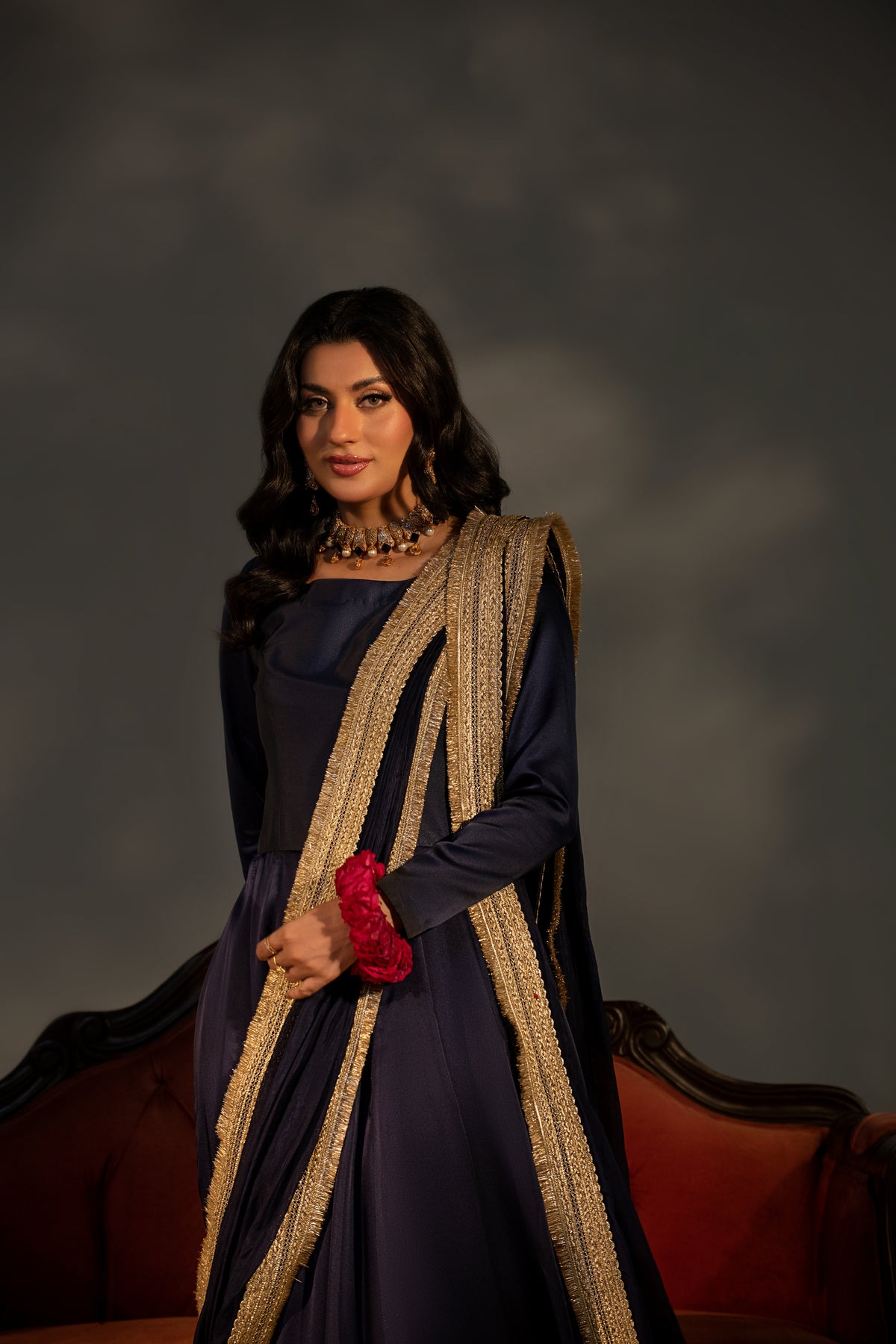 Woman in a dark blue dress with a long, decorative scarf against a dark background