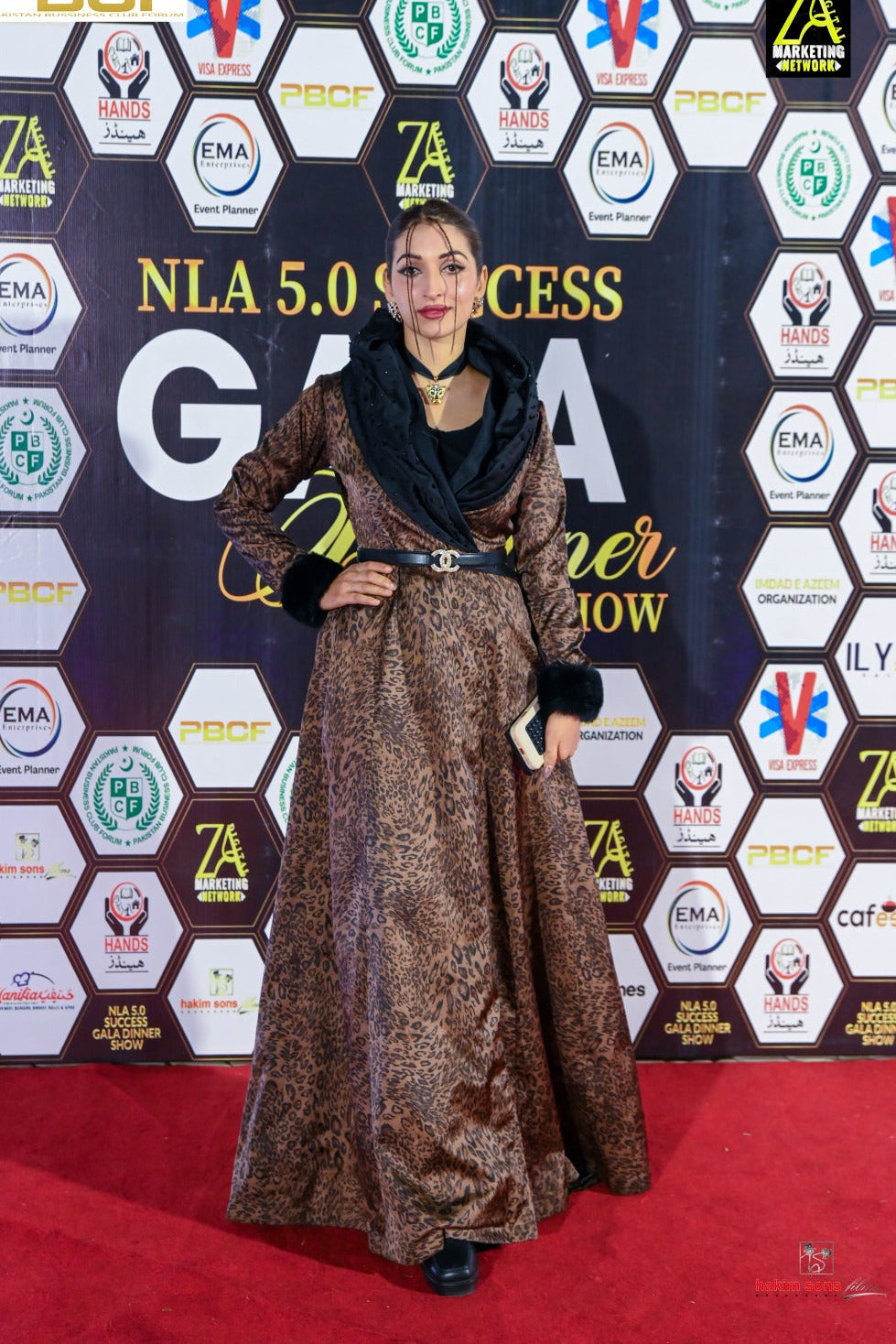 Woman in a patterned dress standing on a red carpet with a branded backdrop