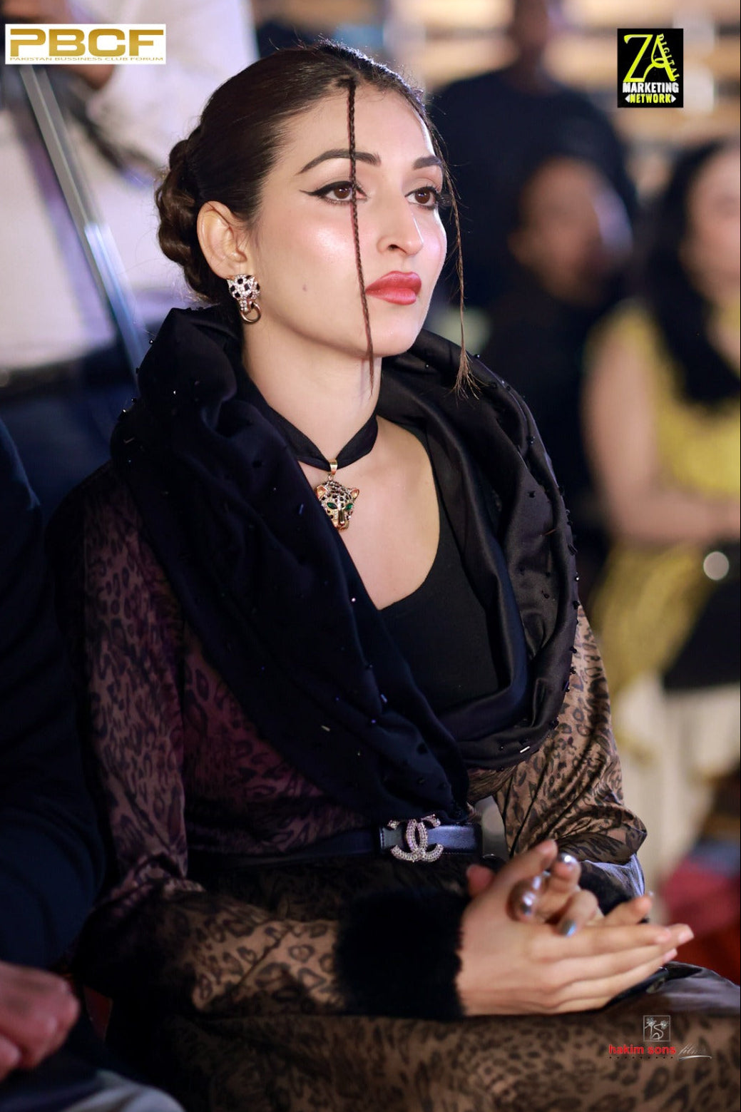 Woman in formal attire with a blurred face, seated in an audience.