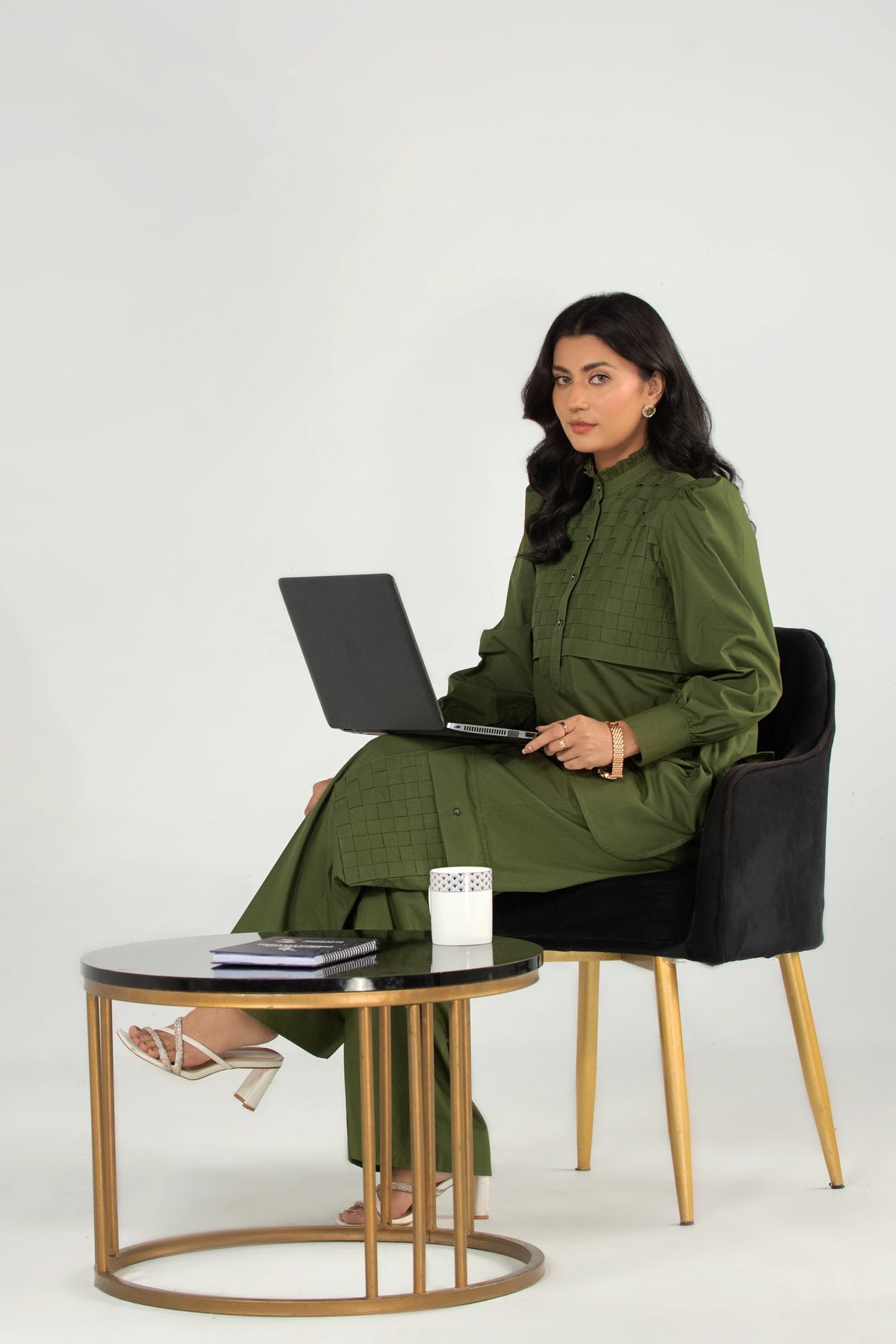 Woman sitting on a chair with a laptop on a small round table against a white background