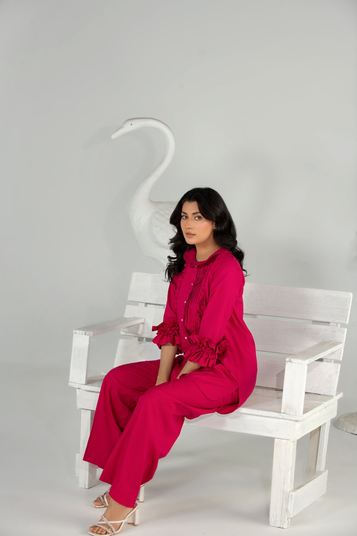 Woman in a bright pink outfit sitting on a white bench with a white swan sculpture in the background.