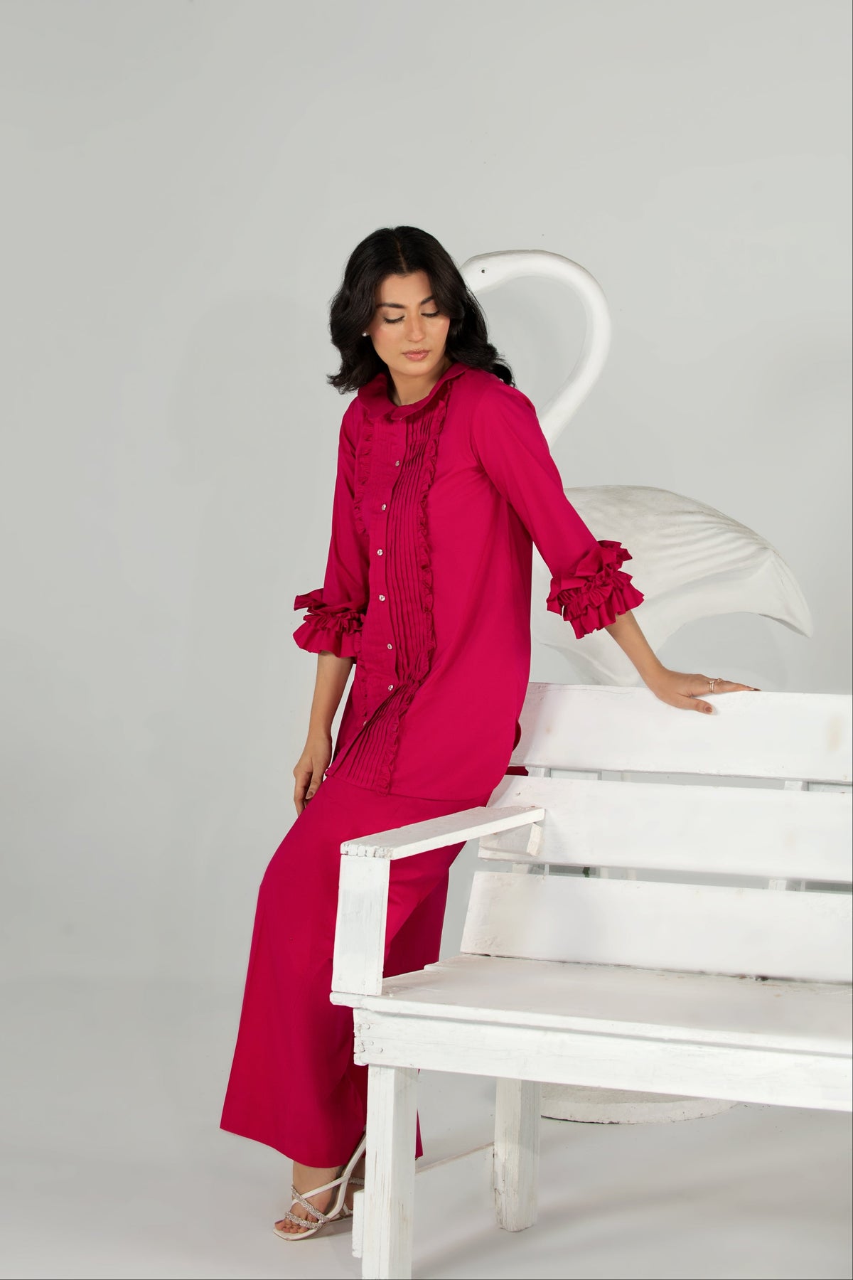 Woman in a bright pink dress sitting on a white chair against a gray background