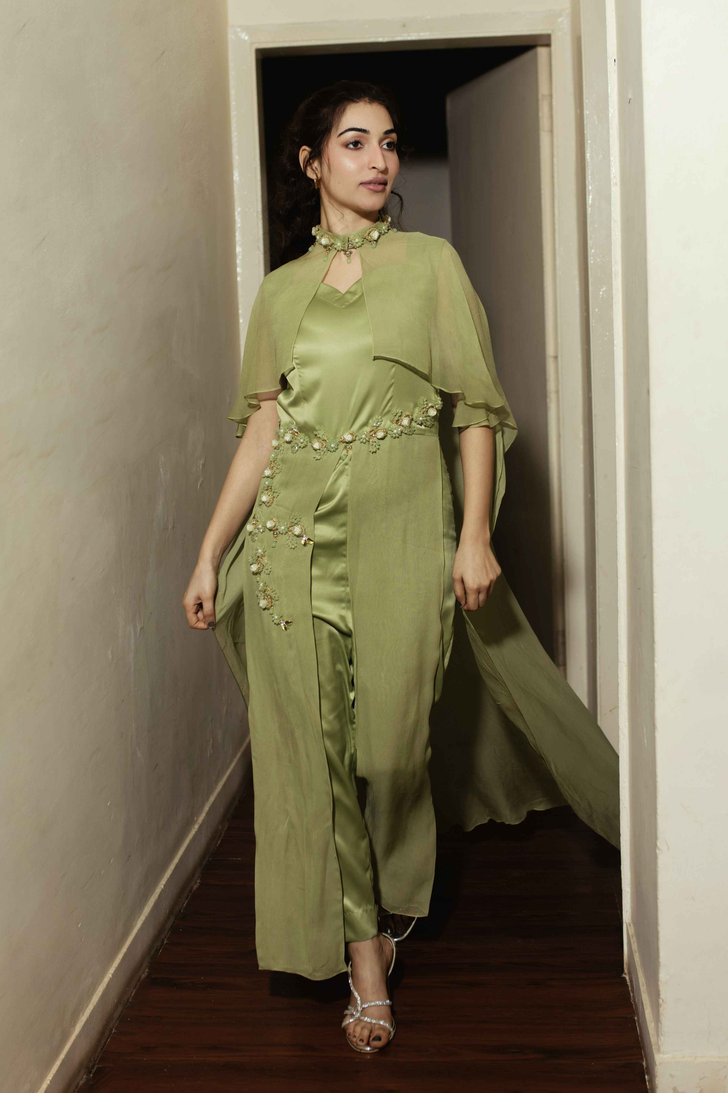 Woman in a green outfit walking through a doorway.