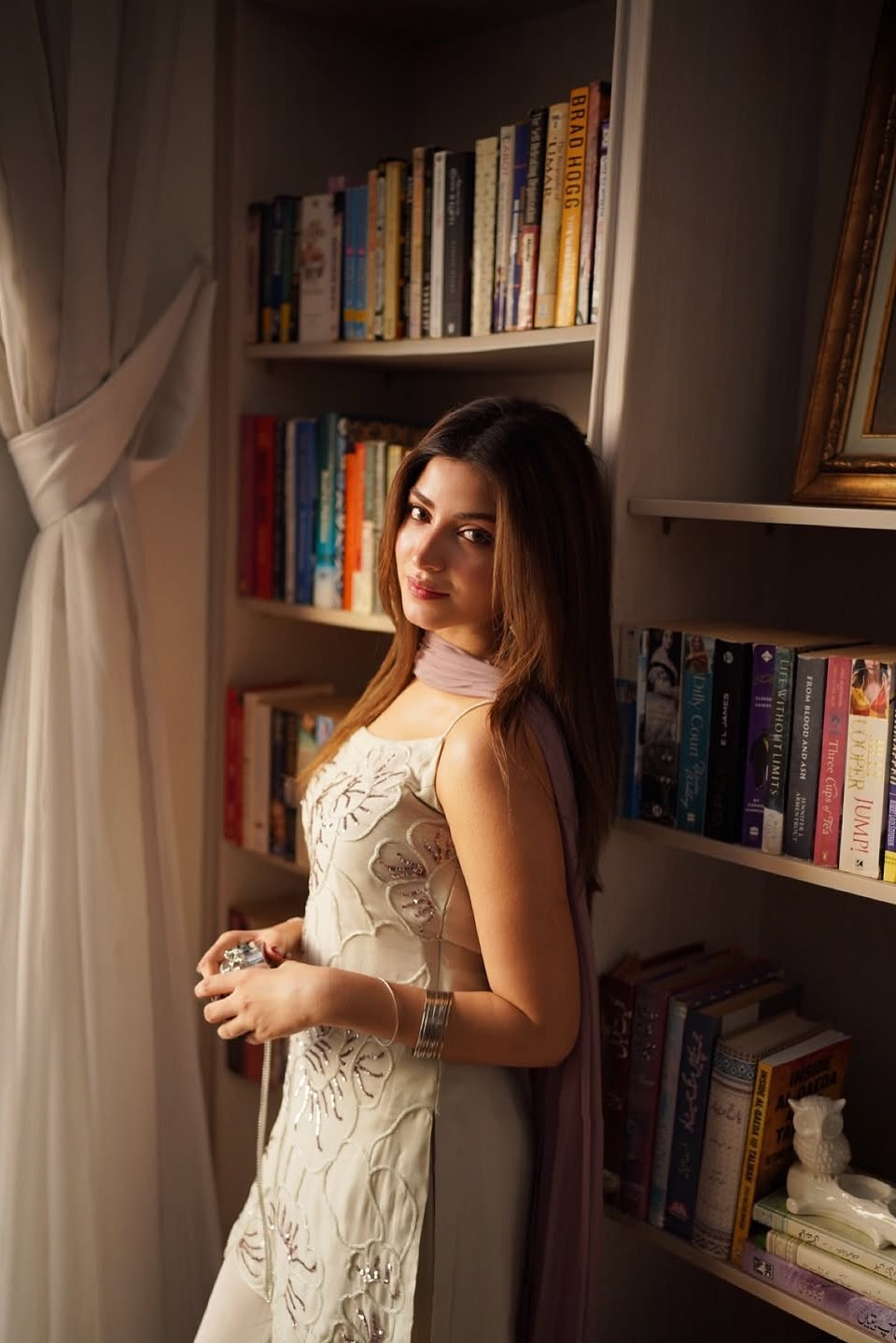 Woman in a white dress standing in a room with bookshelves.