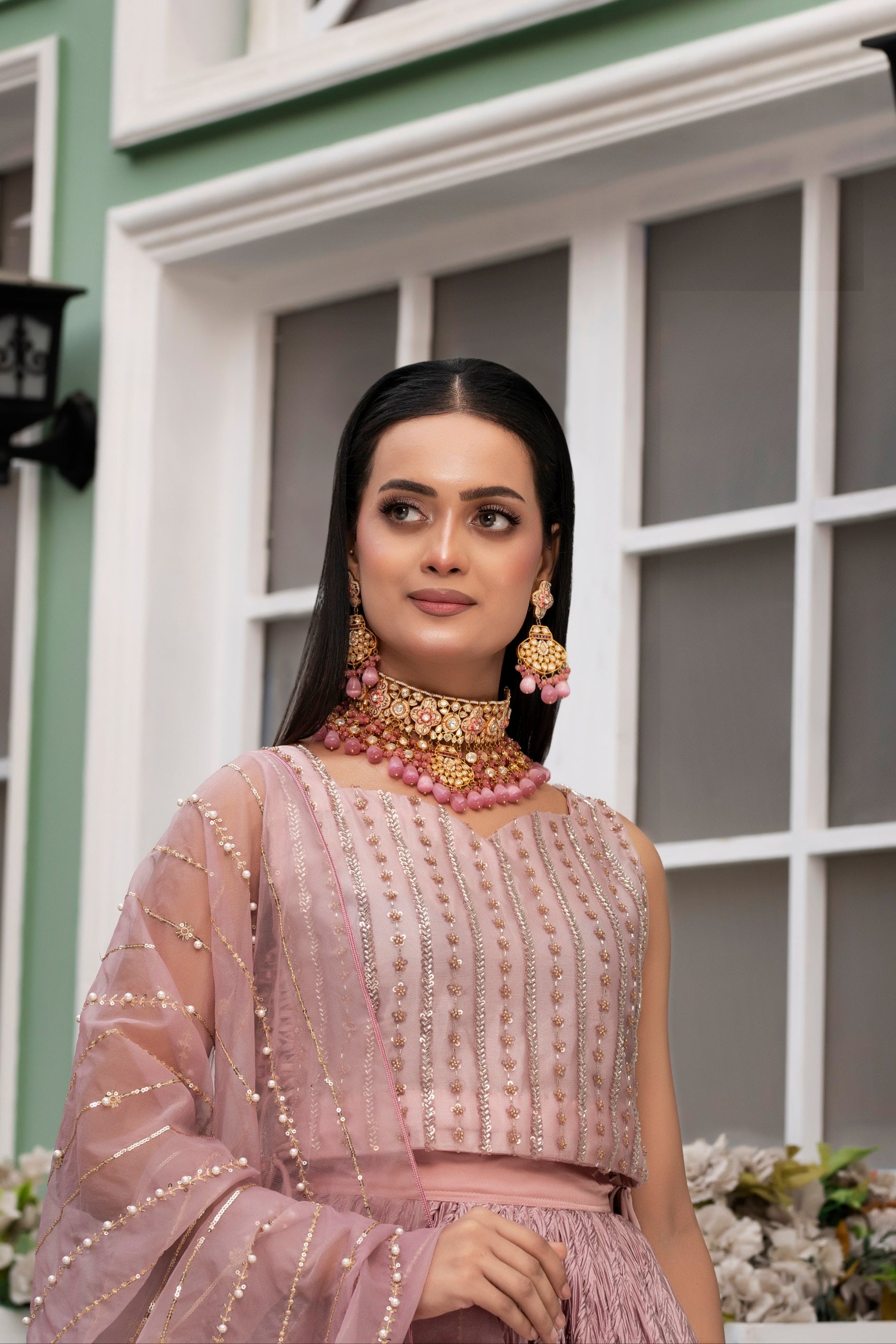 Woman in a pink traditional outfit with gold jewelry standing in front of a building.