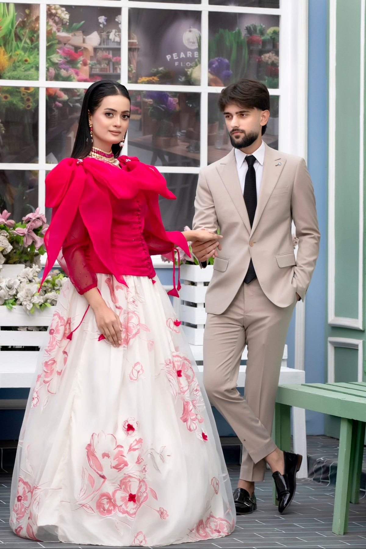 Man and woman in formal attire standing in front of a decorative window with floral patterns.