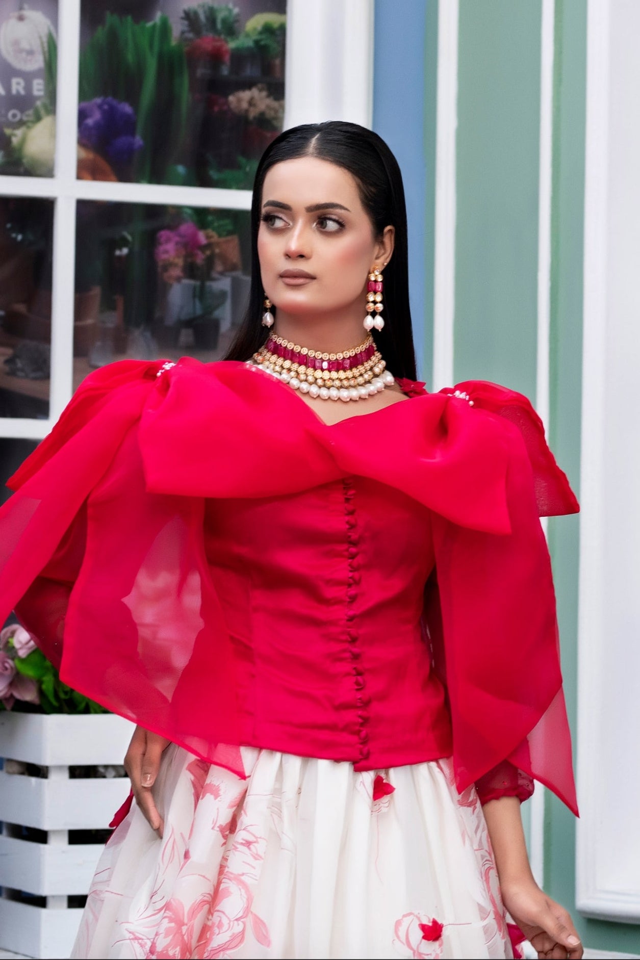 Woman in a red top and white skirt standing in front of a building with large windows.