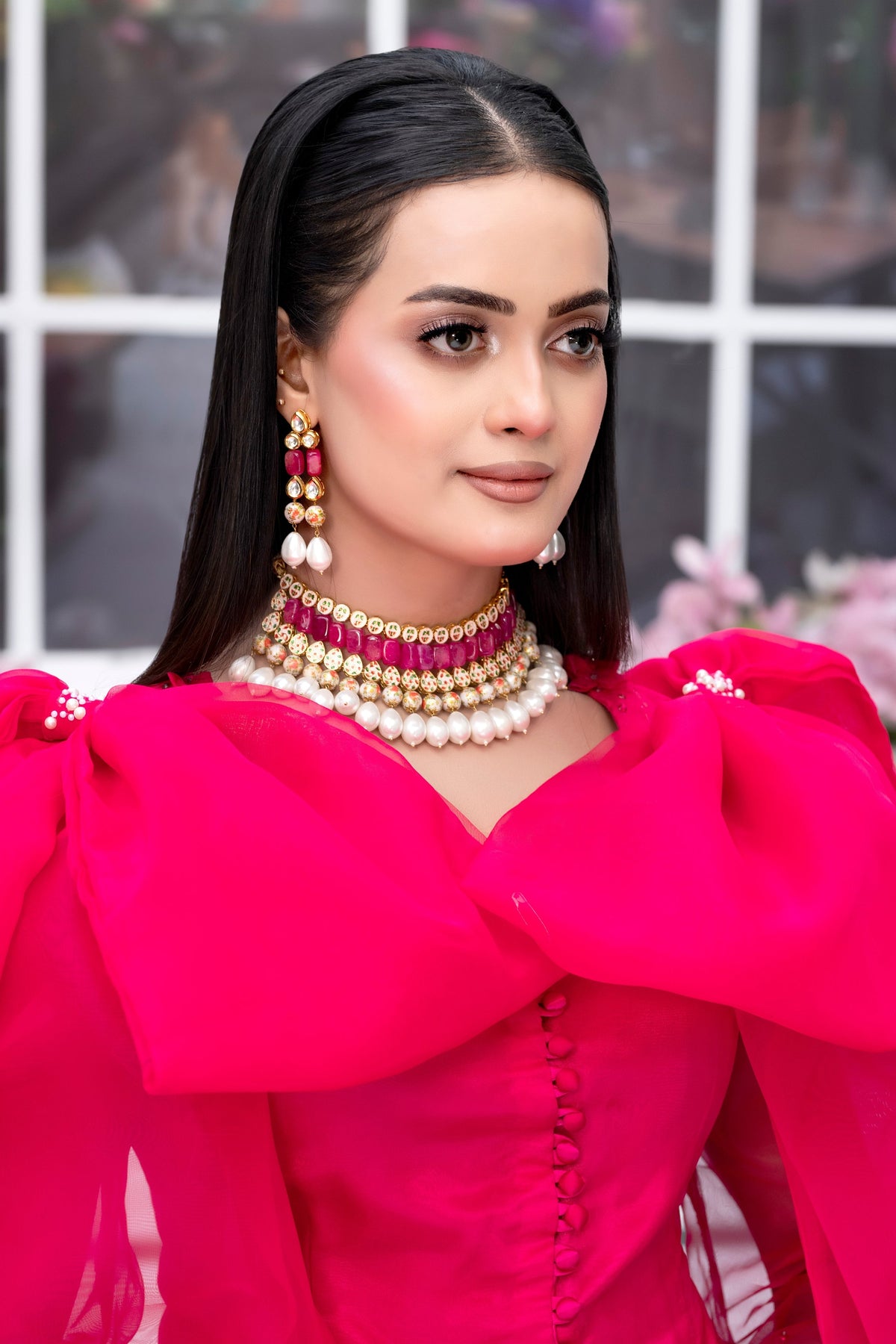 Woman wearing a bright pink outfit with large earrings and a necklace, standing indoors.