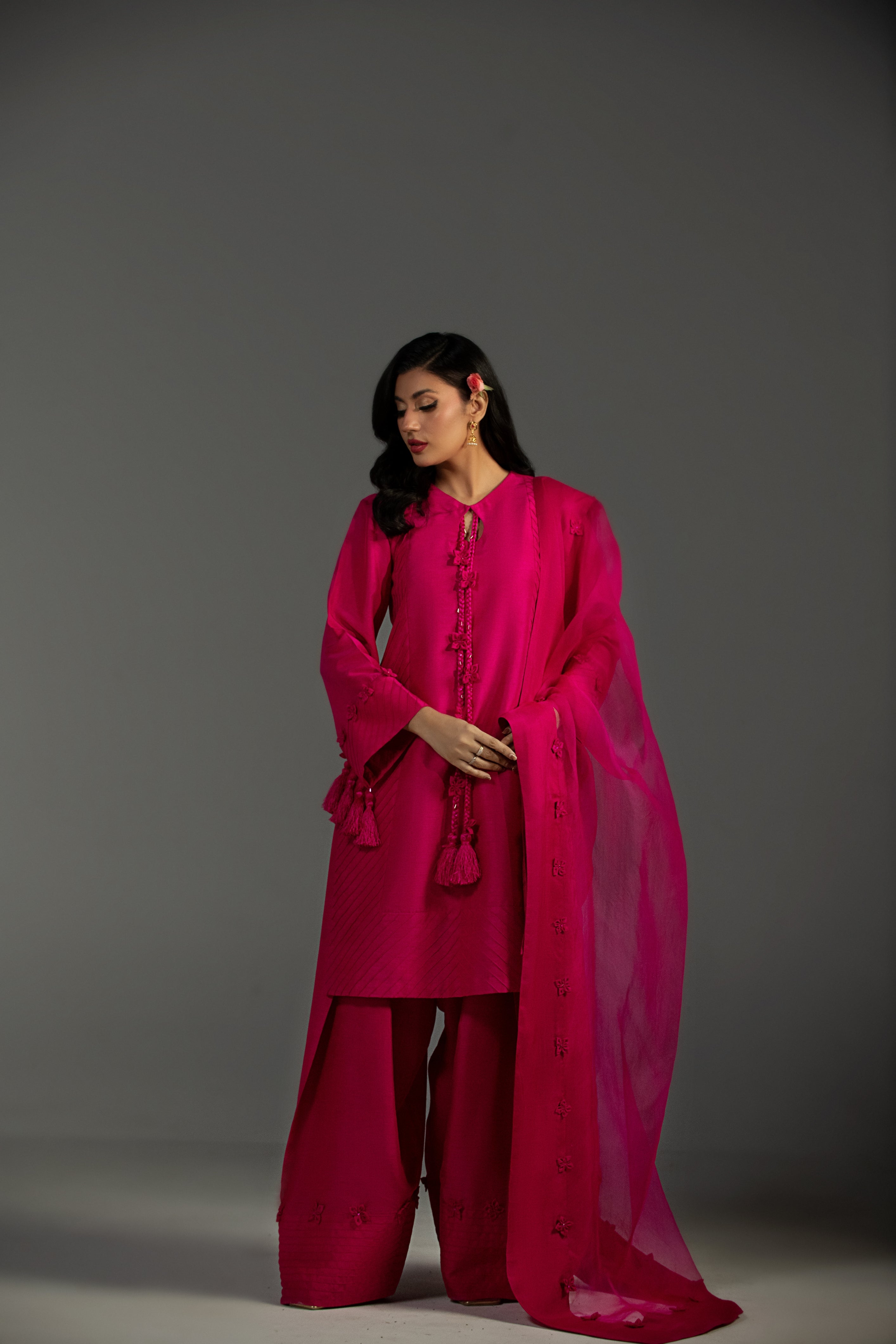 Woman wearing a bright pink traditional outfit with a shawl against a gray background