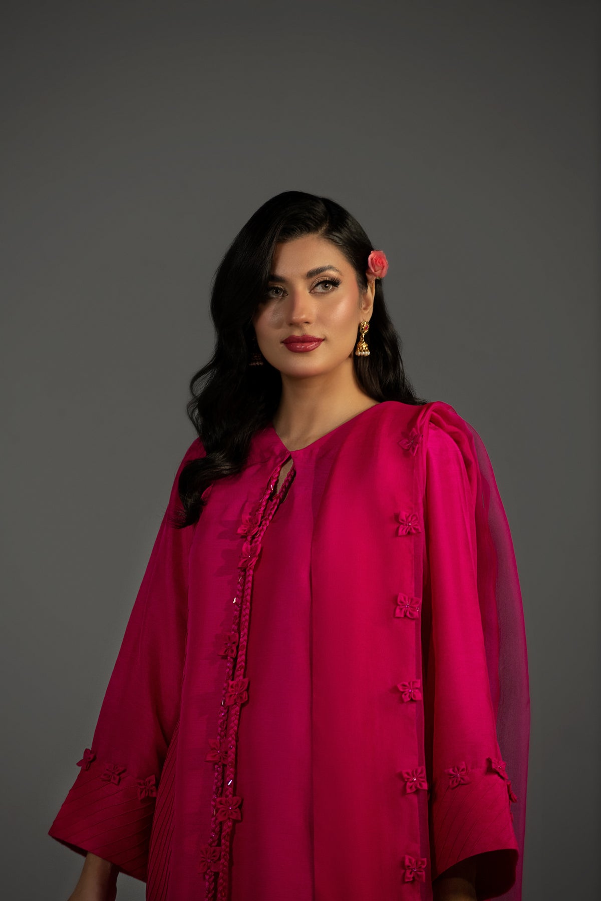 Woman wearing a bright pink traditional outfit against a gray background