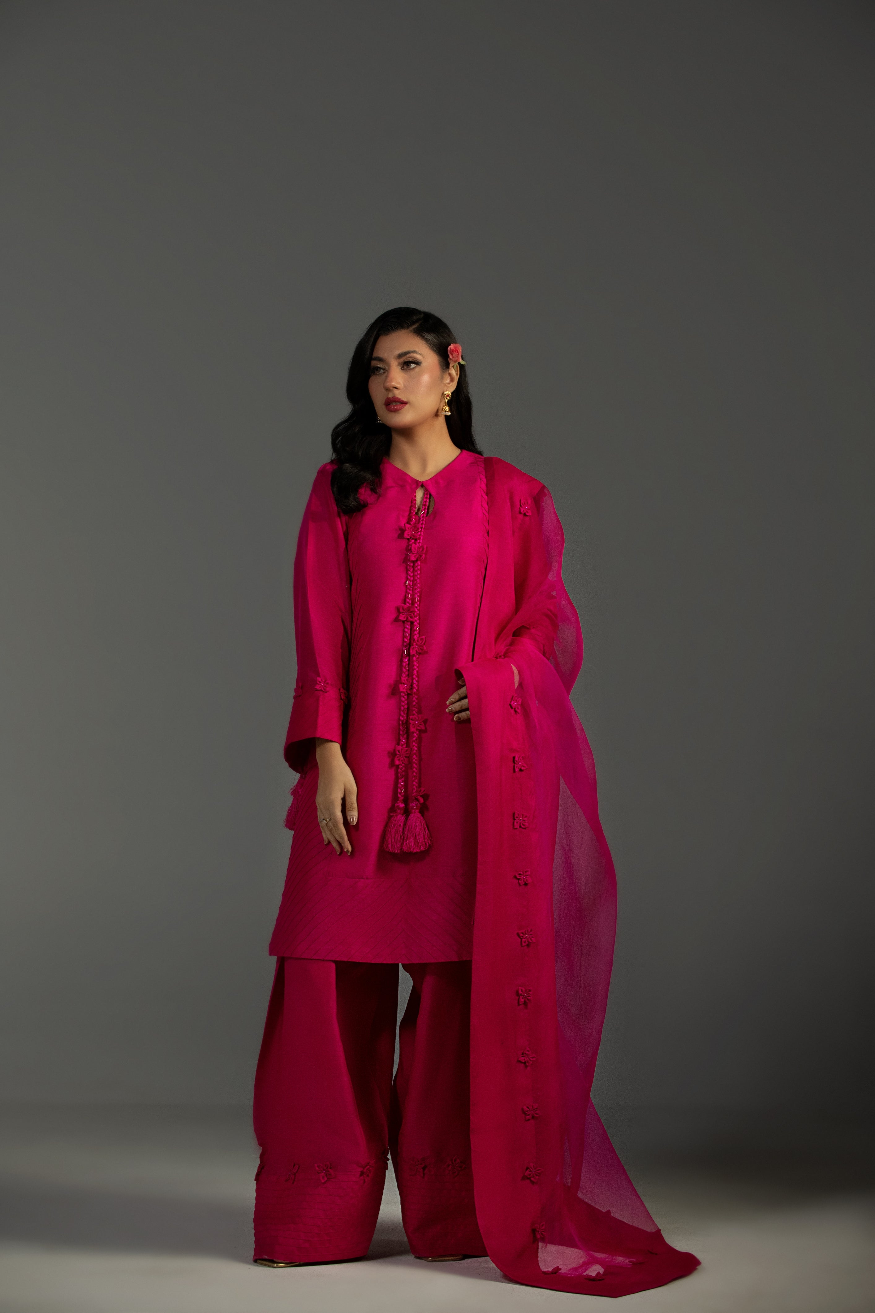 Woman wearing a bright pink traditional outfit with a scarf on a gray background