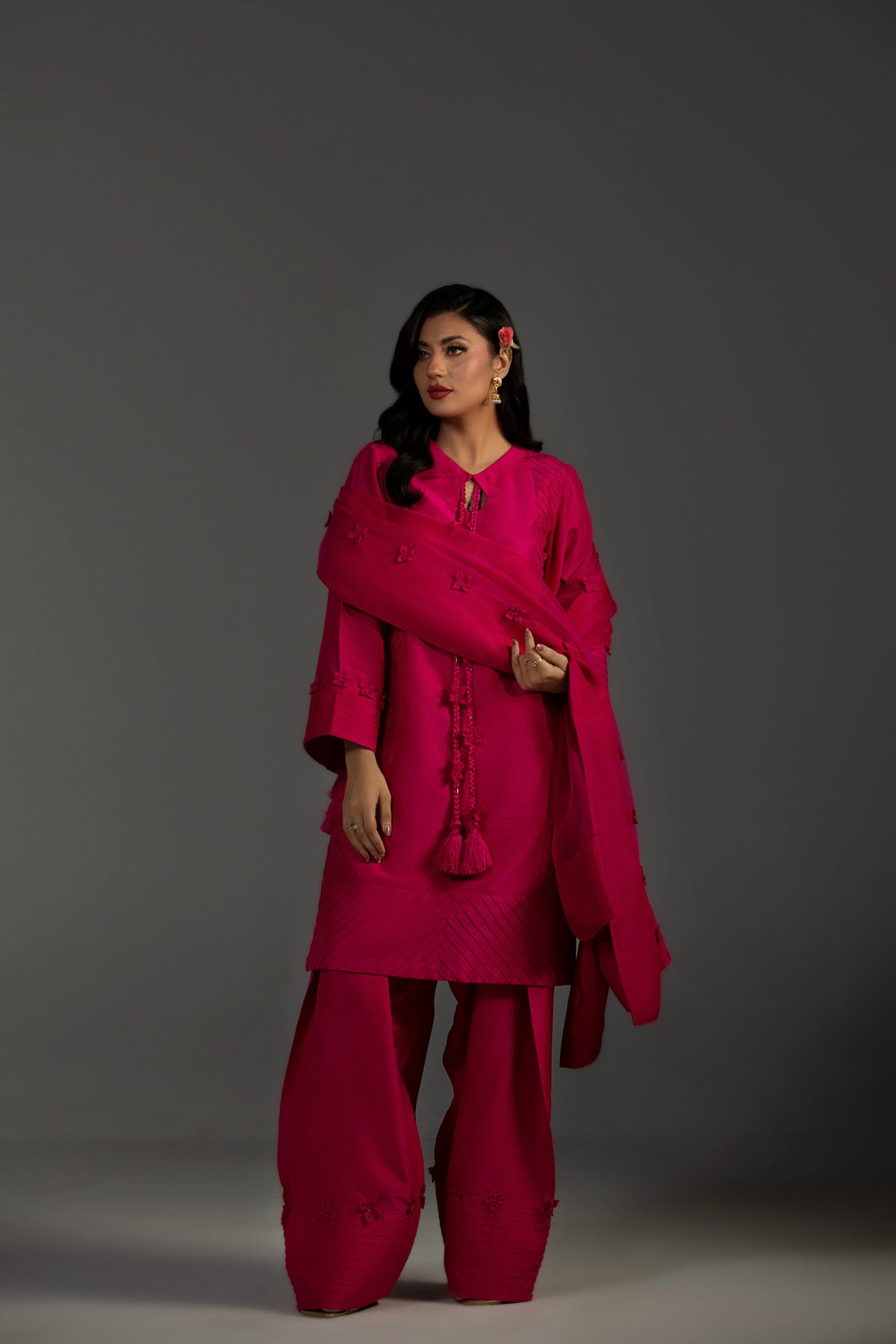 Woman wearing a bright pink traditional outfit with a shawl against a gray background