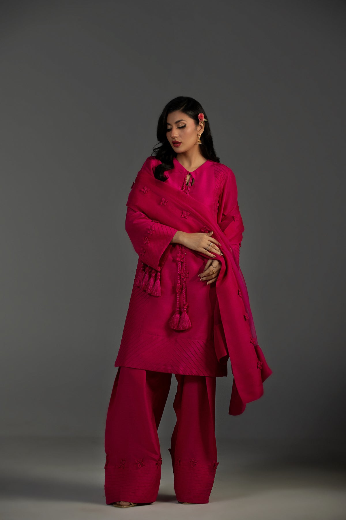 Woman wearing a bright pink traditional outfit with a shawl against a gray background