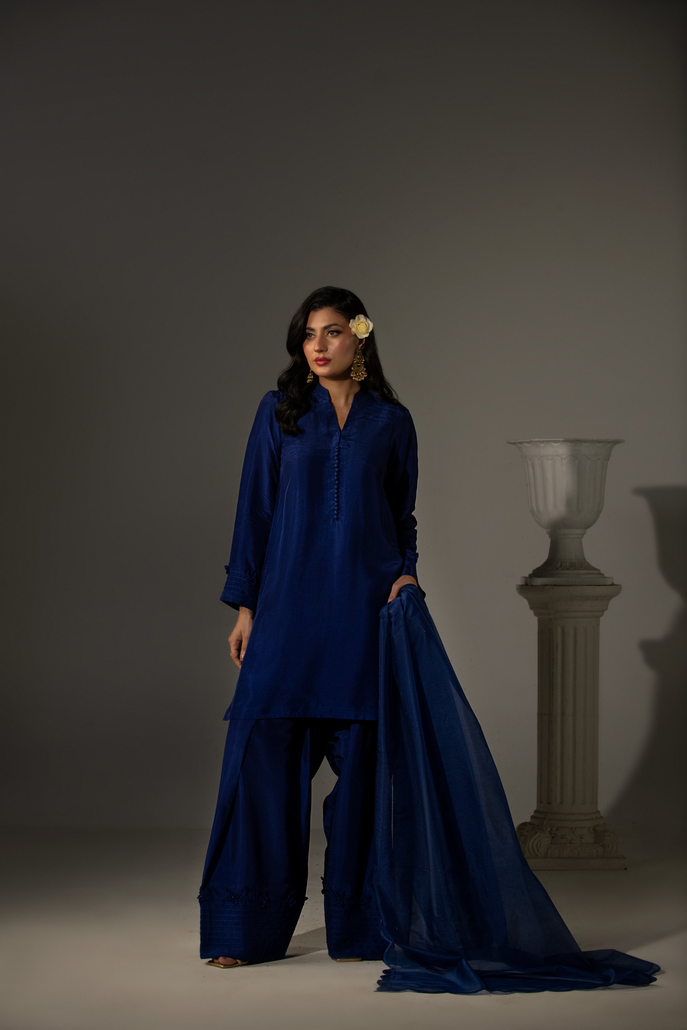 Woman wearing a blue traditional outfit with a draped fabric against a gray background