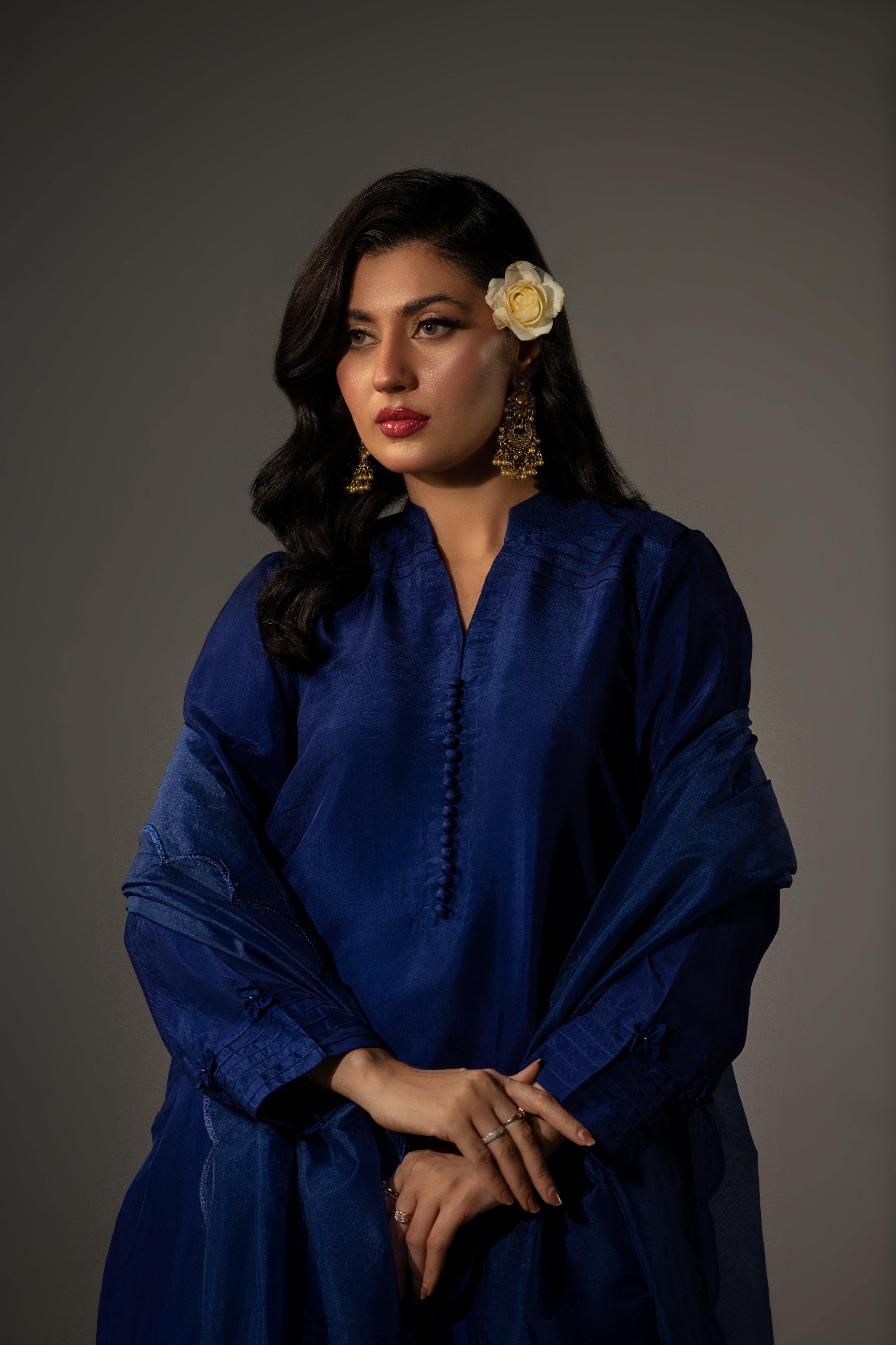 Woman wearing a blue outfit with a flower in her hair against a gray background