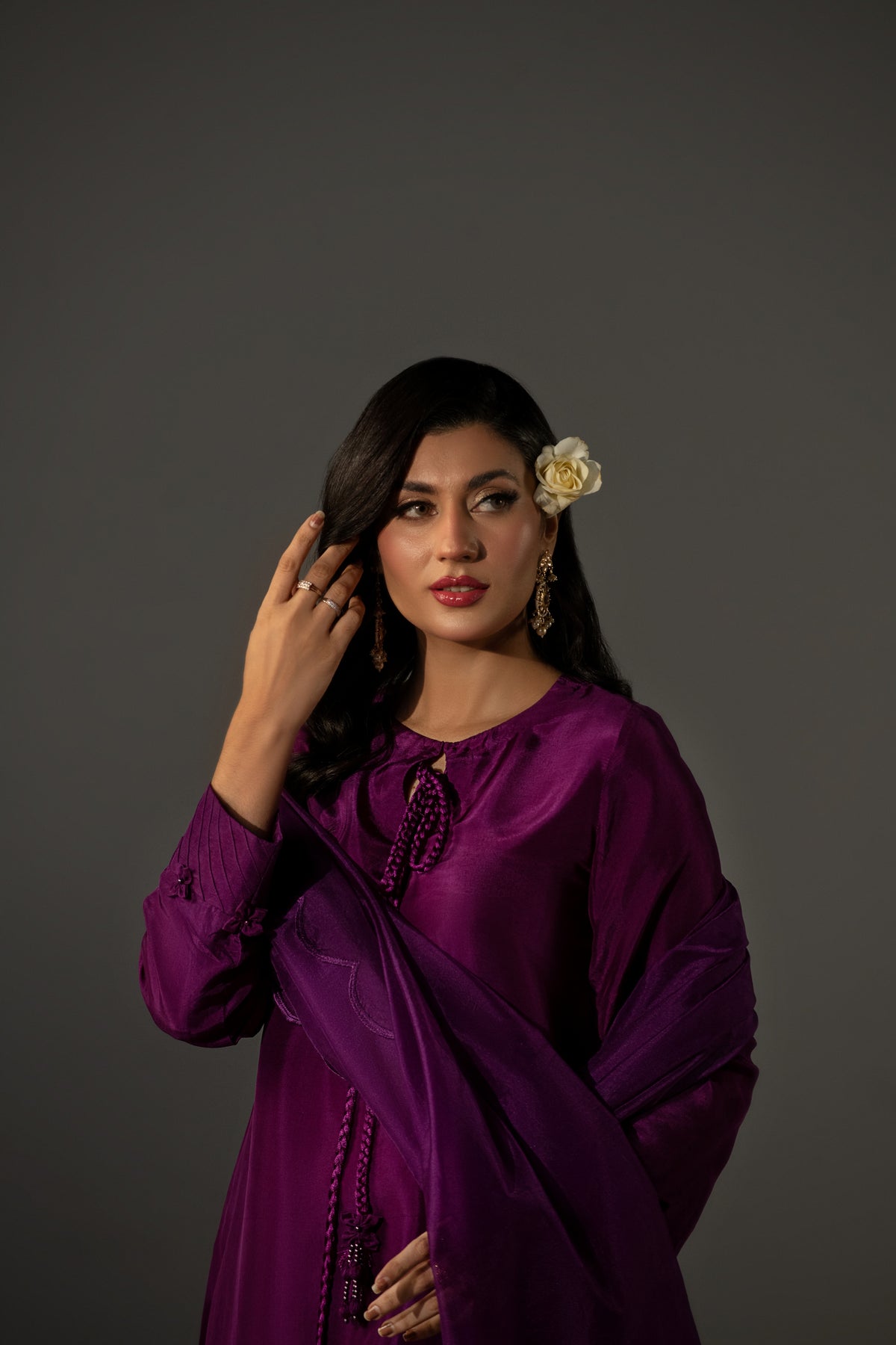 Woman in a purple traditional outfit with a flower in her hair against a gray background