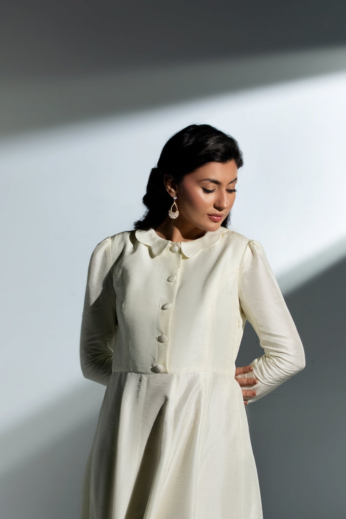 Woman wearing a white outfit with a high collar against a gray background