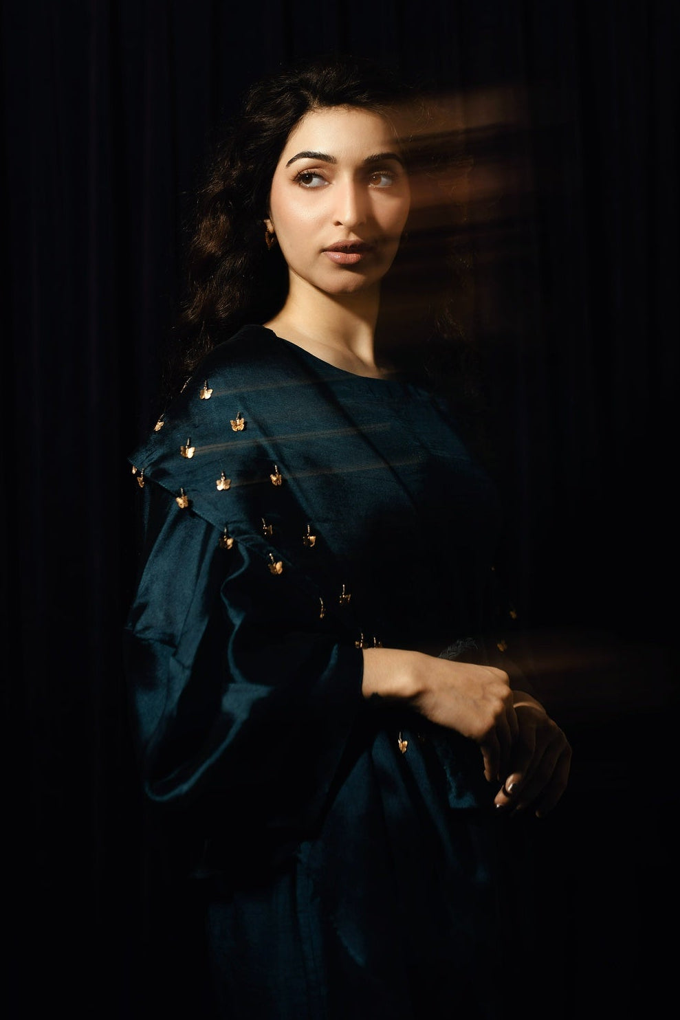 Woman wearing a dark blue dress with gold embellishments against a black background