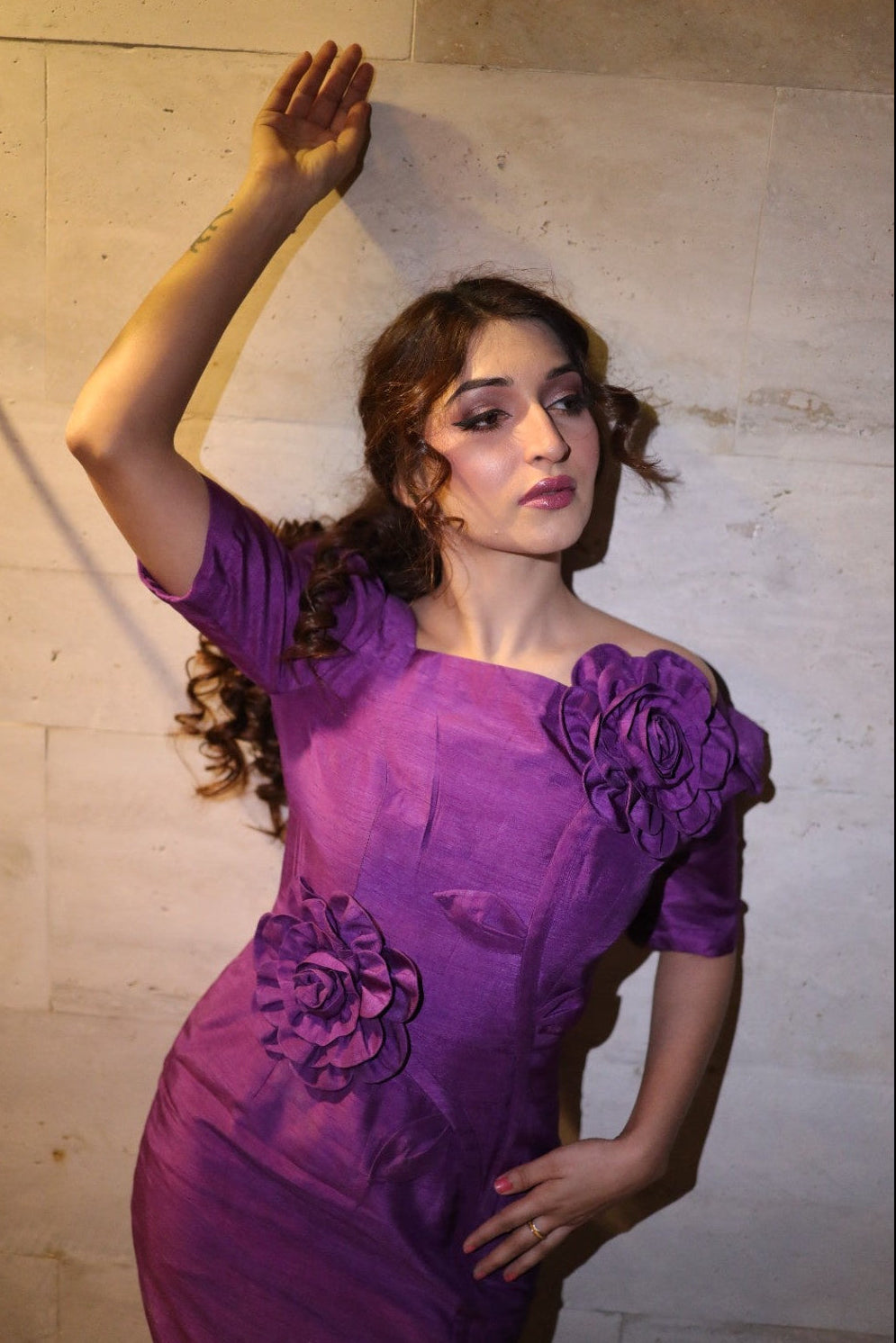 Woman in a purple dress with floral details against a textured wall.