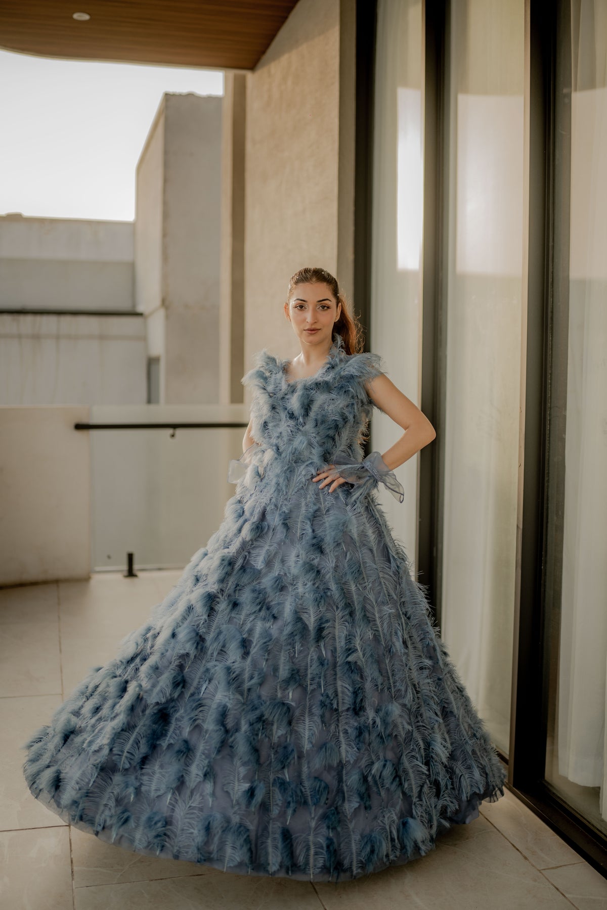 Woman in a blue floral dress standing indoors with large windows.
