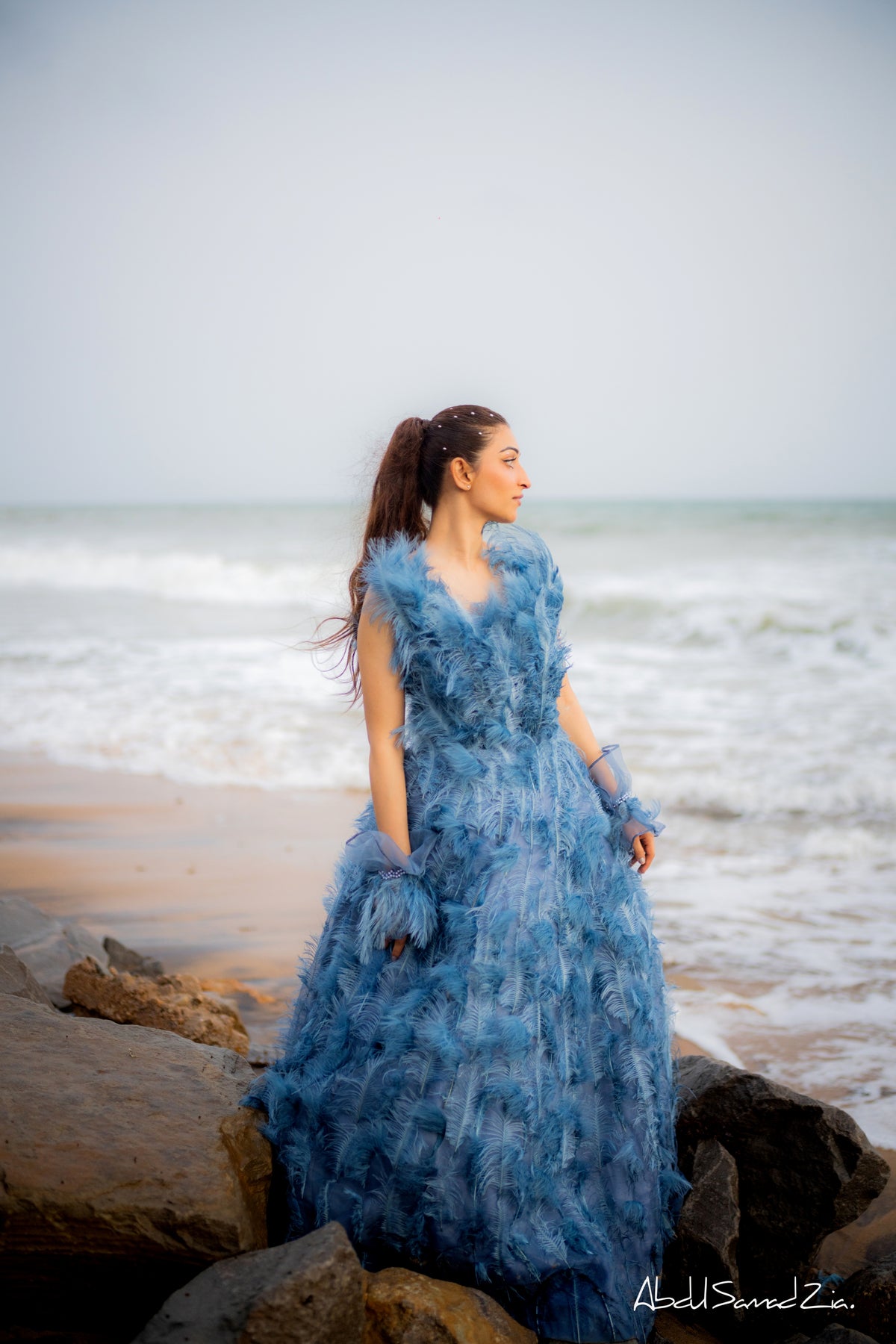 Woman in a blue dress standing on a beach with ocean waves in the background