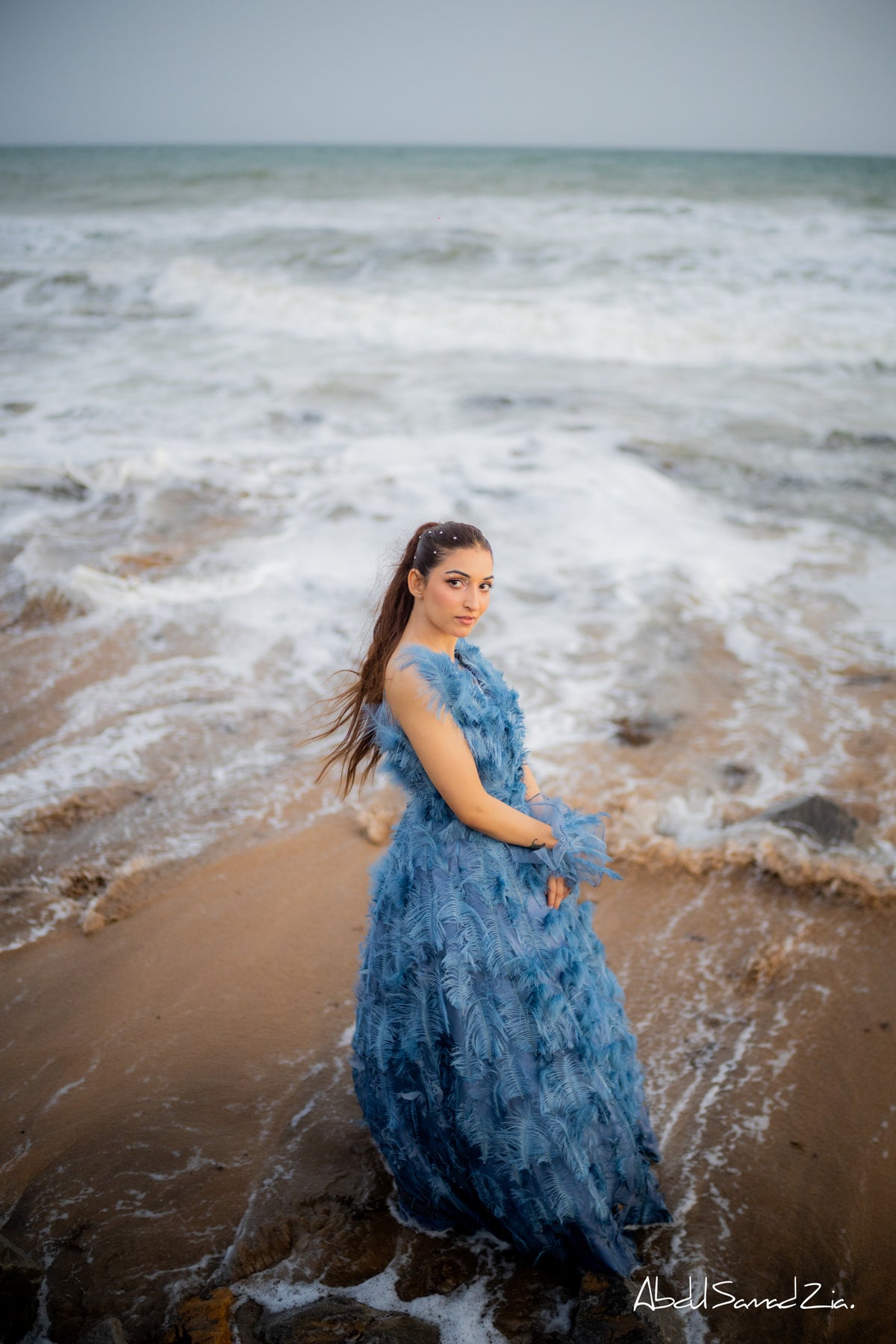 Woman in a blue dress standing on a beach with waves in the background