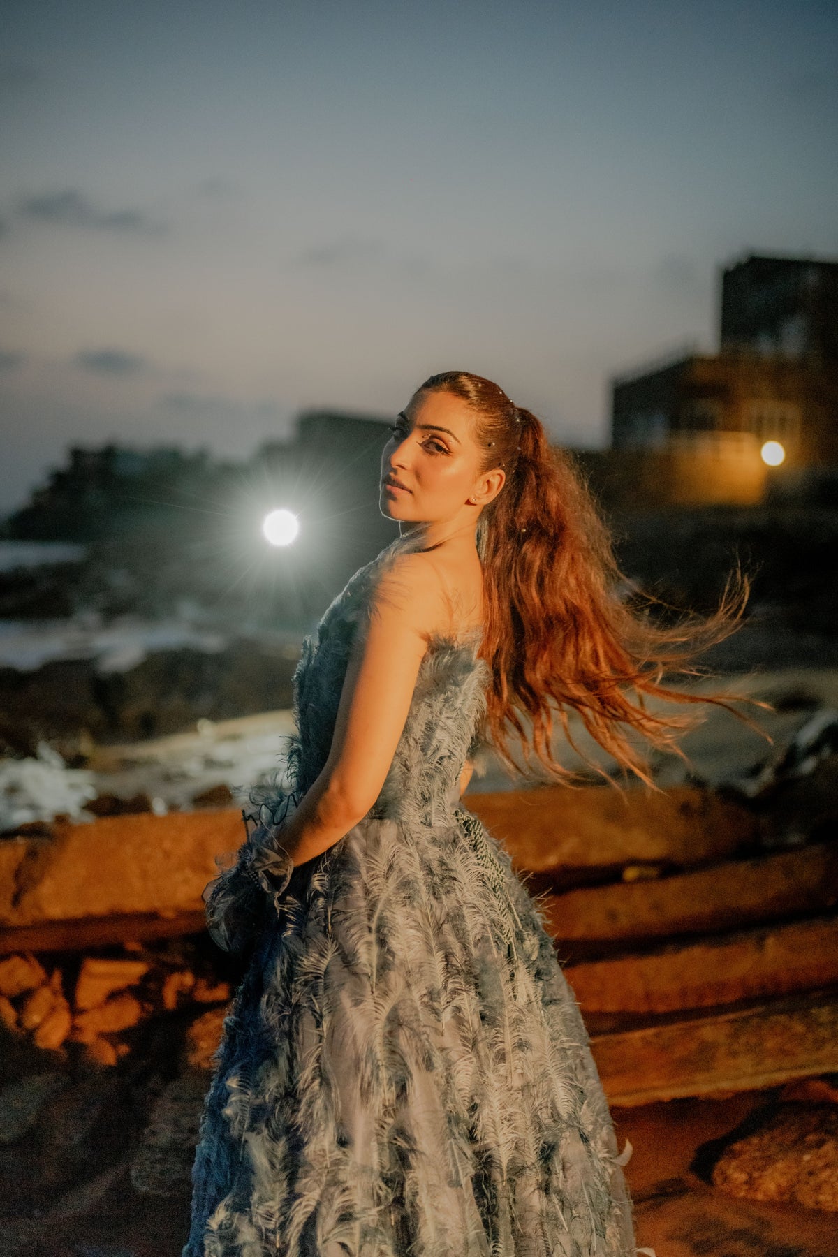 Woman in a strapless dress with long hair standing on a rocky ledge at night.