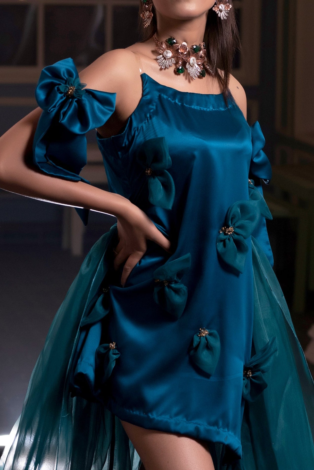 Woman wearing a teal dress with floral details in an indoor setting