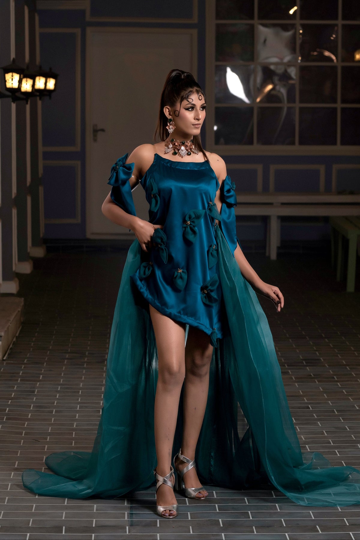 Woman in a teal dress standing in an indoor setting with chandeliers.