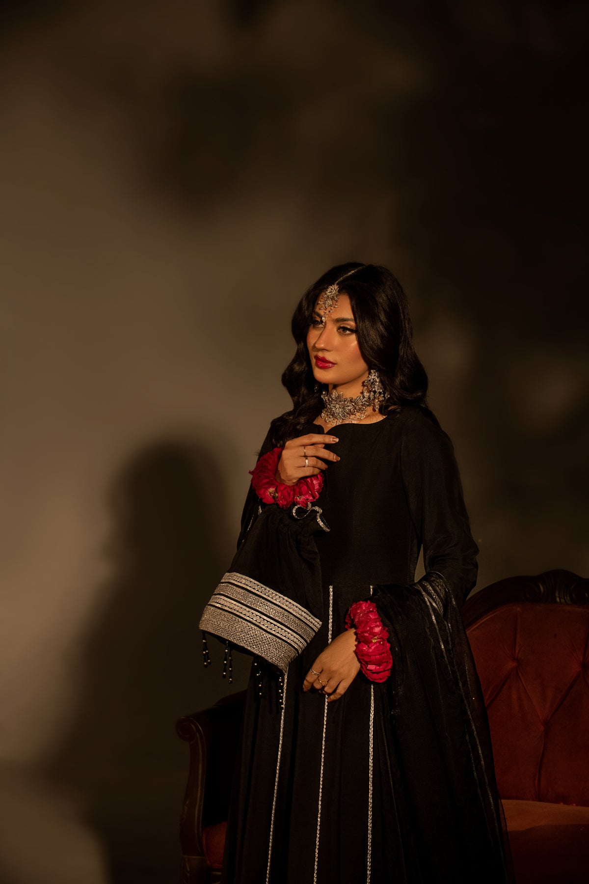 Woman in a black traditional outfit with red and silver details against a dark background