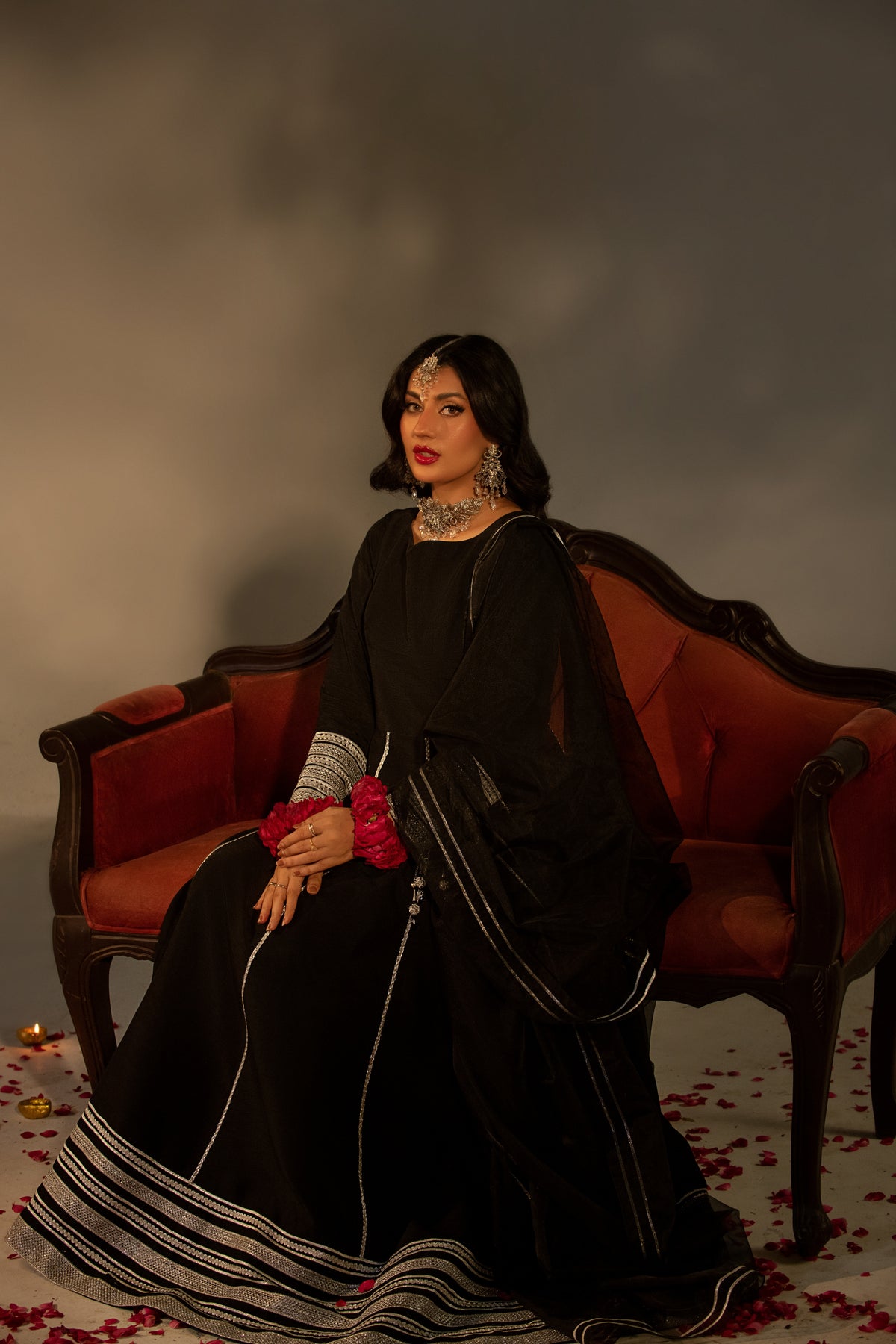 Woman in a black dress sitting on a red couch with a dark, moody background