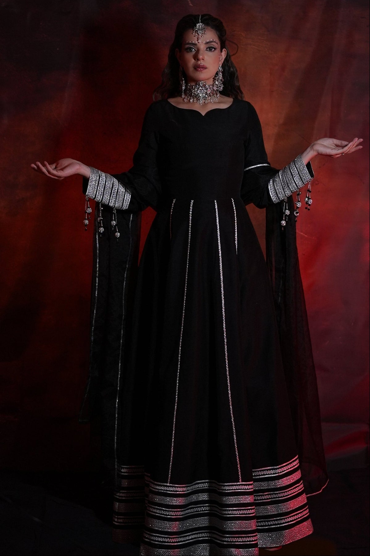 Woman in a black traditional outfit with silver accents against a dark background