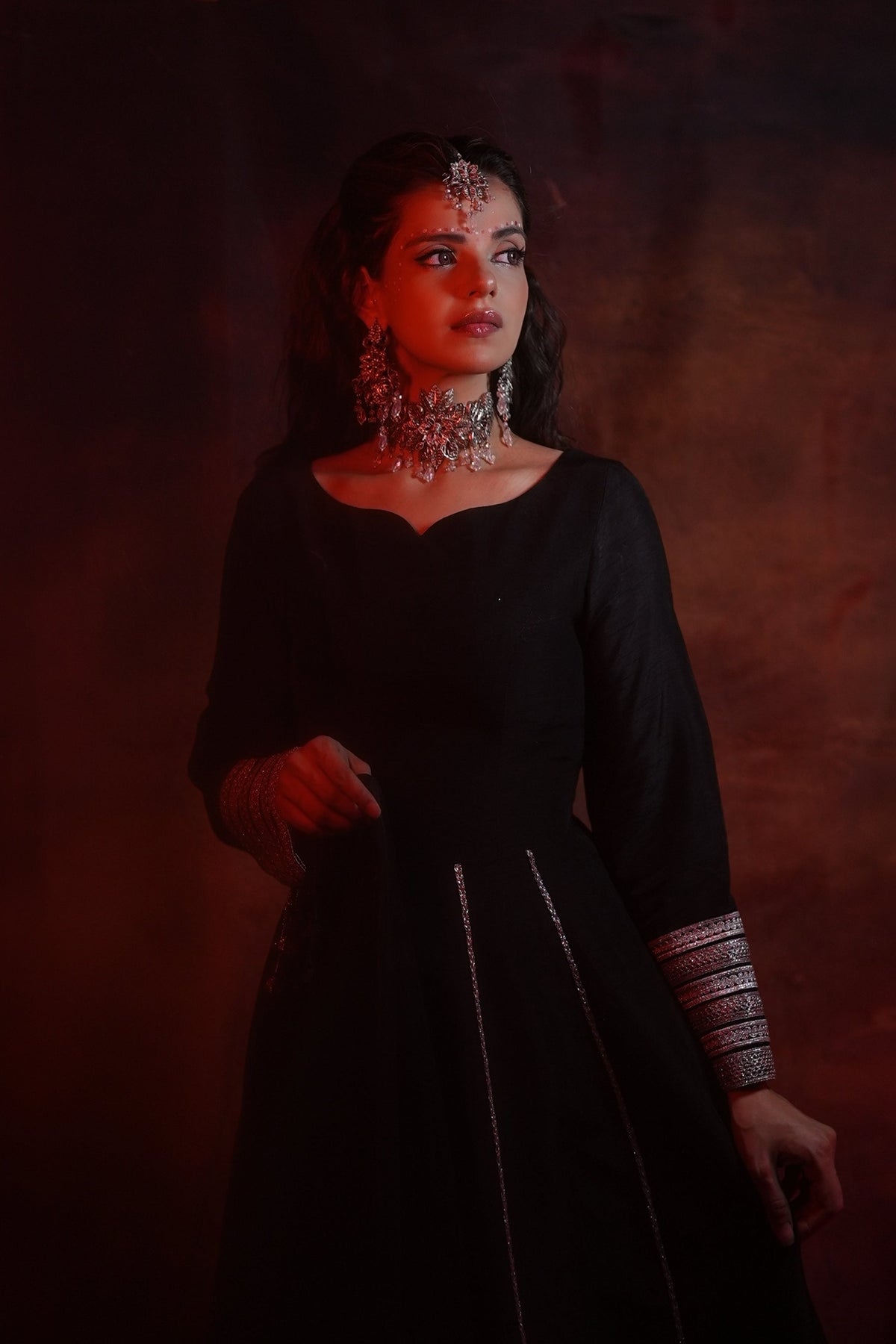 Woman in a black dress with jewelry against a dark background