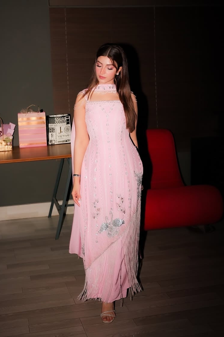 Woman in a pink dress standing in a room with a table and decorative items.