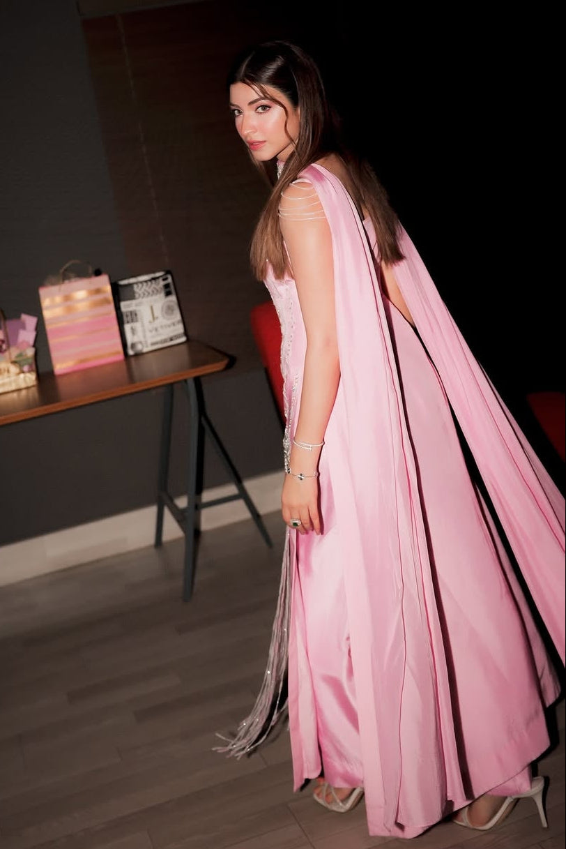 Woman in a pink saree standing in a room with a table and decorative items.