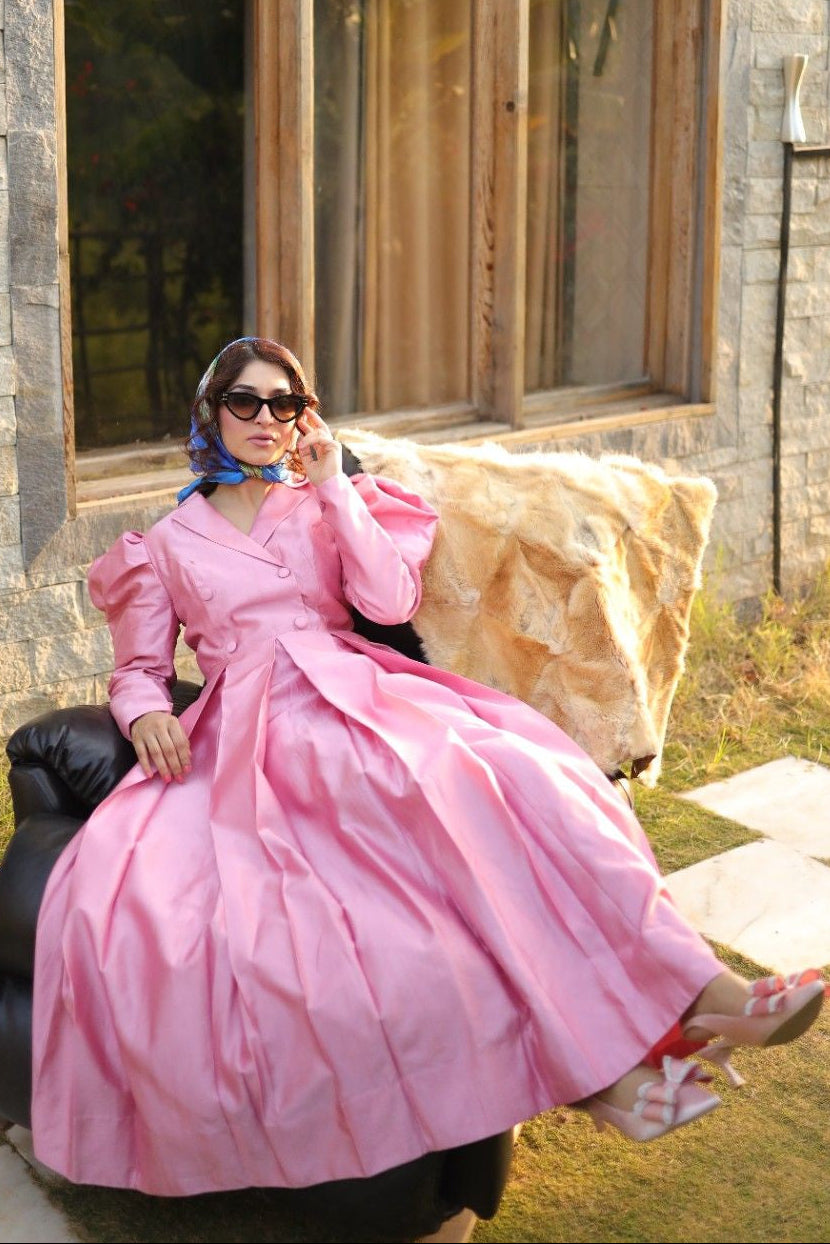 Woman in a pink dress sitting on a stone wall with a building in the background