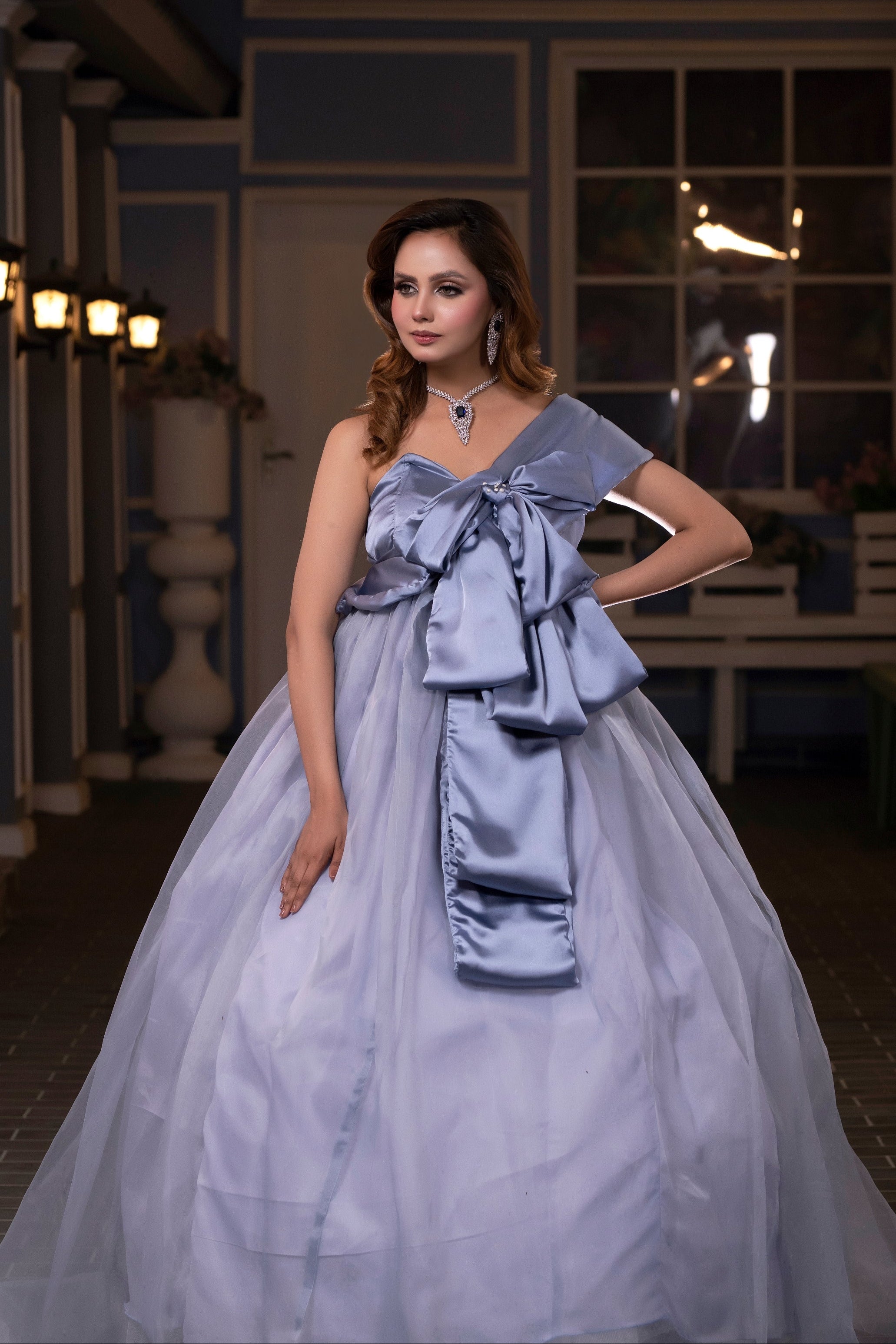Woman in a light blue gown standing in an indoor setting with decorative lights.