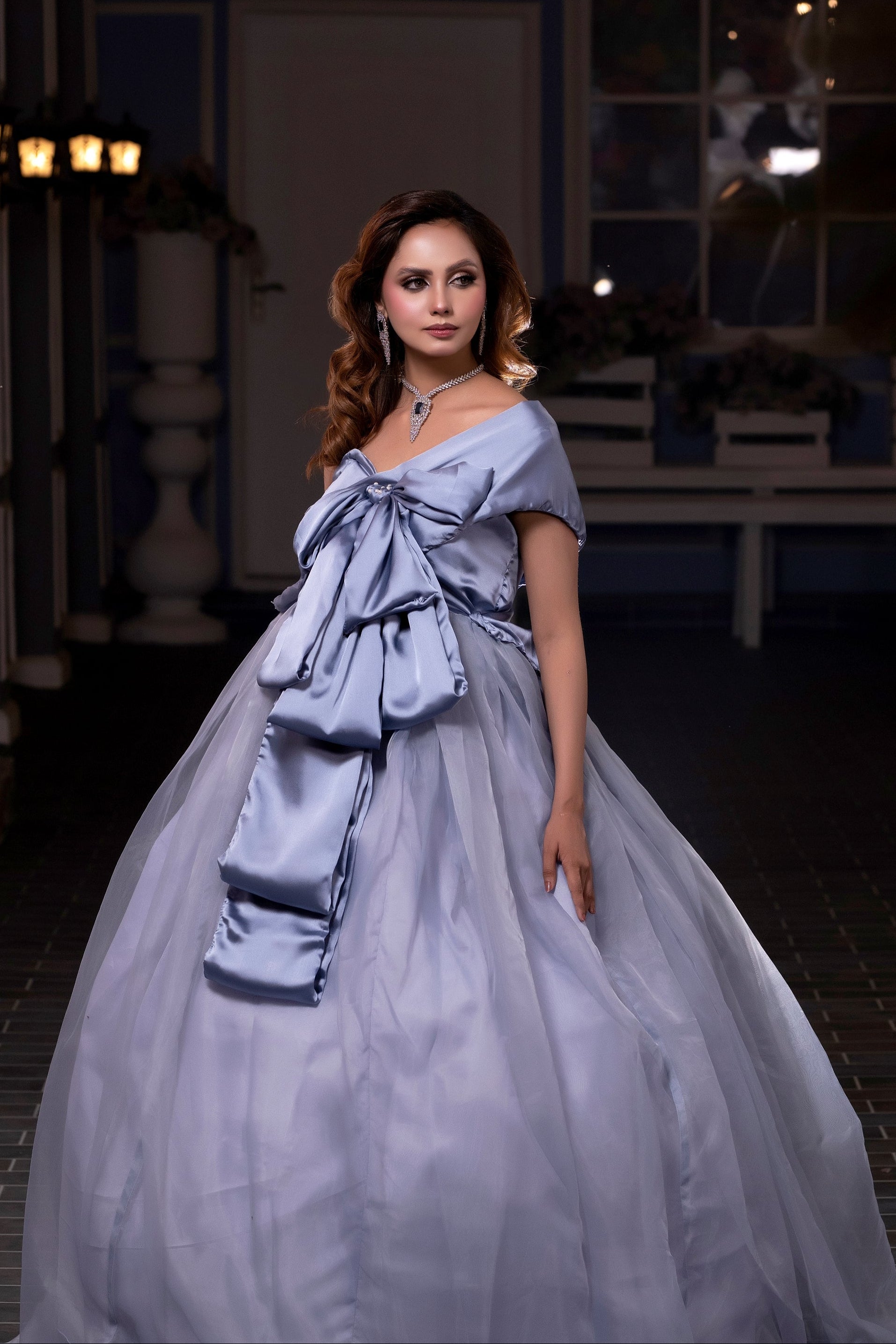 Woman in a light blue gown standing in a dimly lit room with decorative elements.