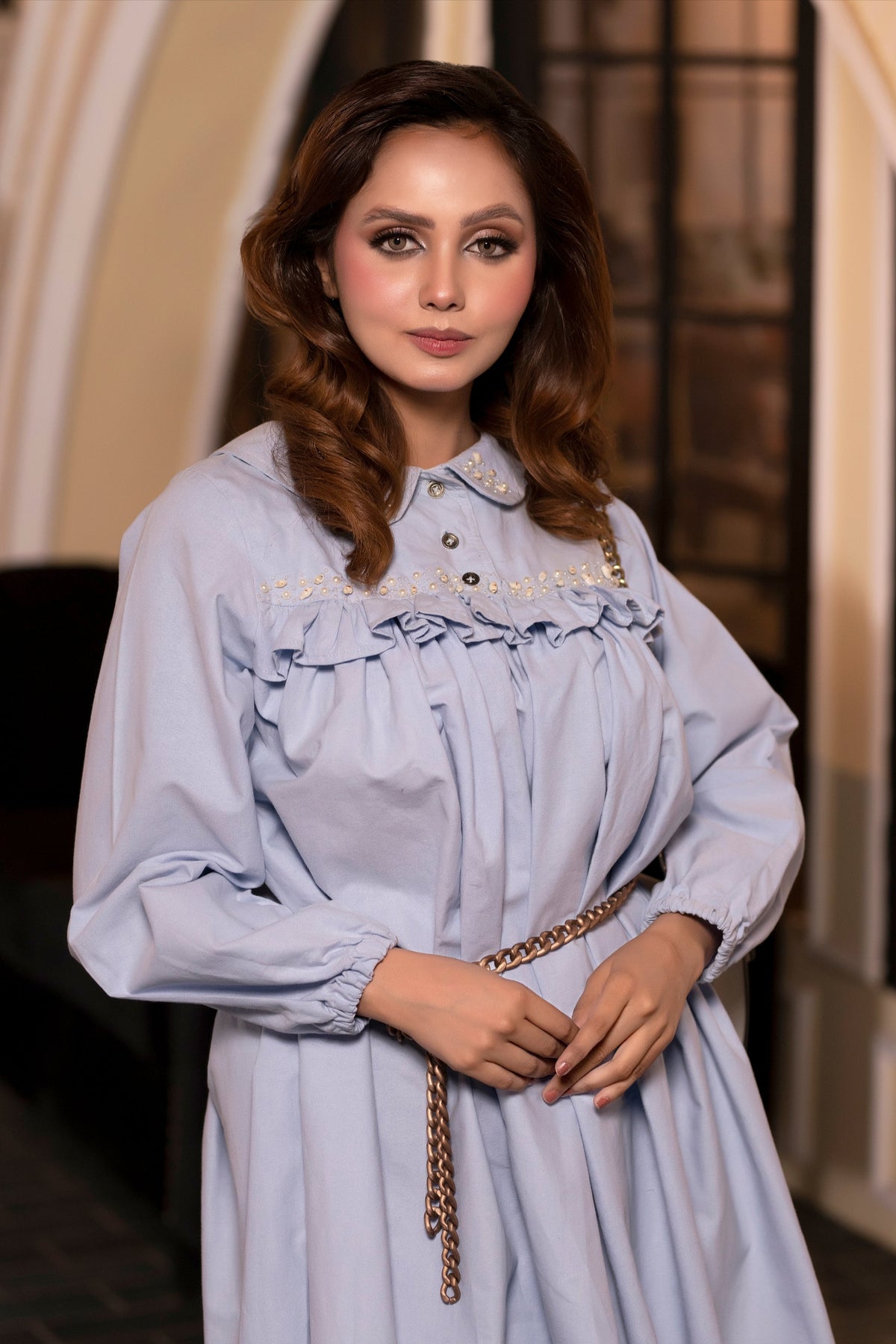 Woman wearing a light blue dress with a gold belt in an indoor setting