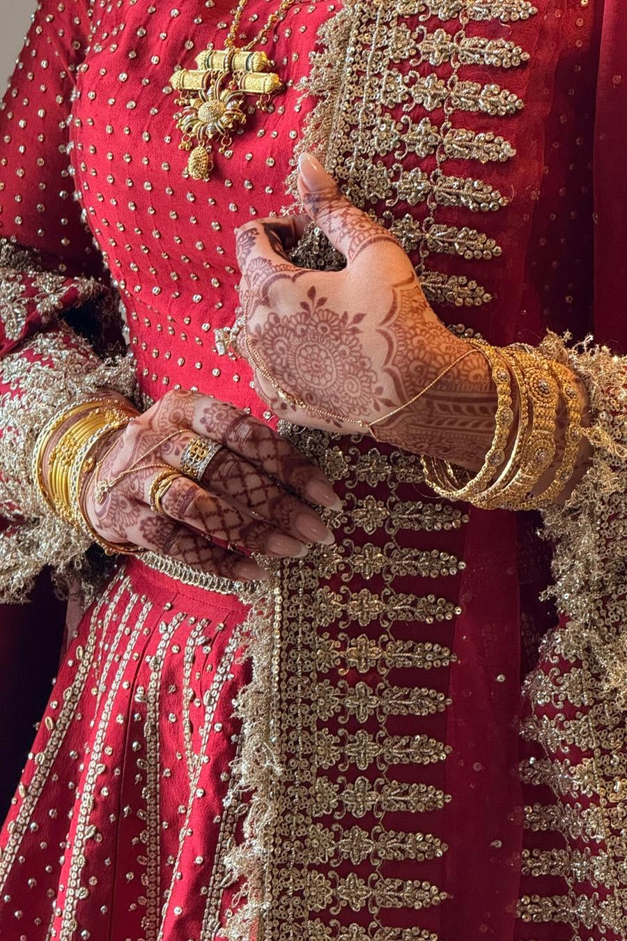 Close-up of a person in traditional red and gold attire with intricate henna designs on hands.