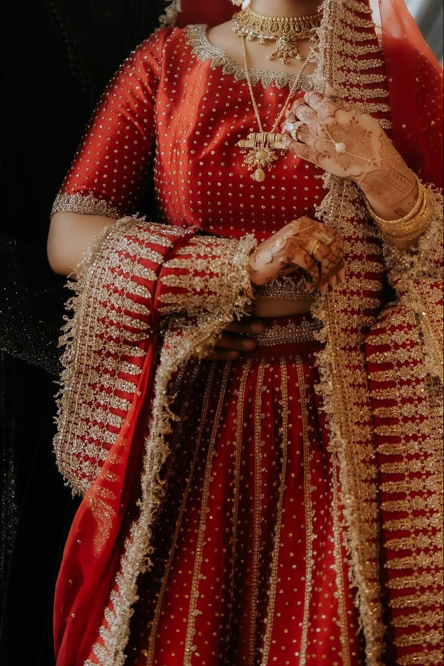 Person wearing a red traditional outfit with gold embroidery and jewelry.